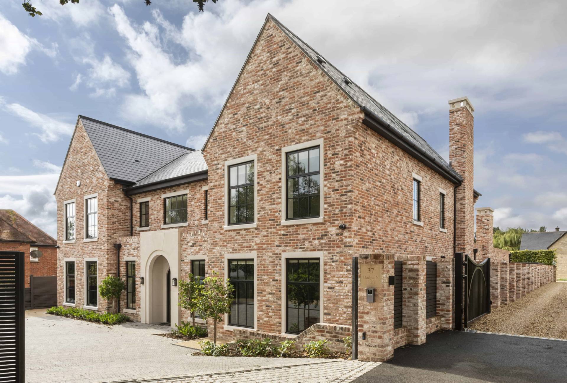 Modern country estate location home hero cover image in Buckinghamshire, HP18 featuring red brick facade, outdoor heated swimming pool, dark navy lounge with orange velvet sofa, golf simulator room, and crittall extension, the ultimate high-visibility backdrop for feature film productions, TV drama filming, luxury brand campaigns, and commercial photography via Love Locations.
