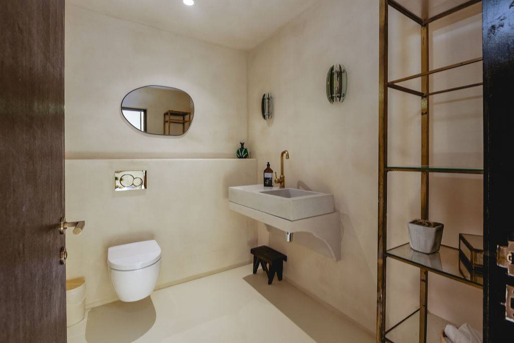 Minimalist bathroom with a white wall-mounted sink, floating toilet, and microcement plaster walls, Love Locations GU32.