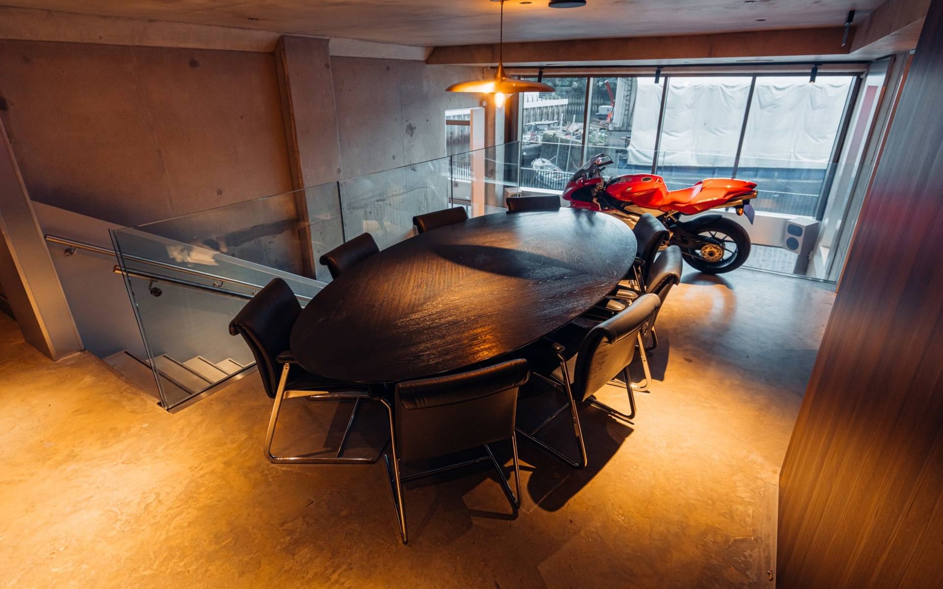 Elegant boardroom or private dining setup with a oval wooden table and motorcycle display through Love Locations.