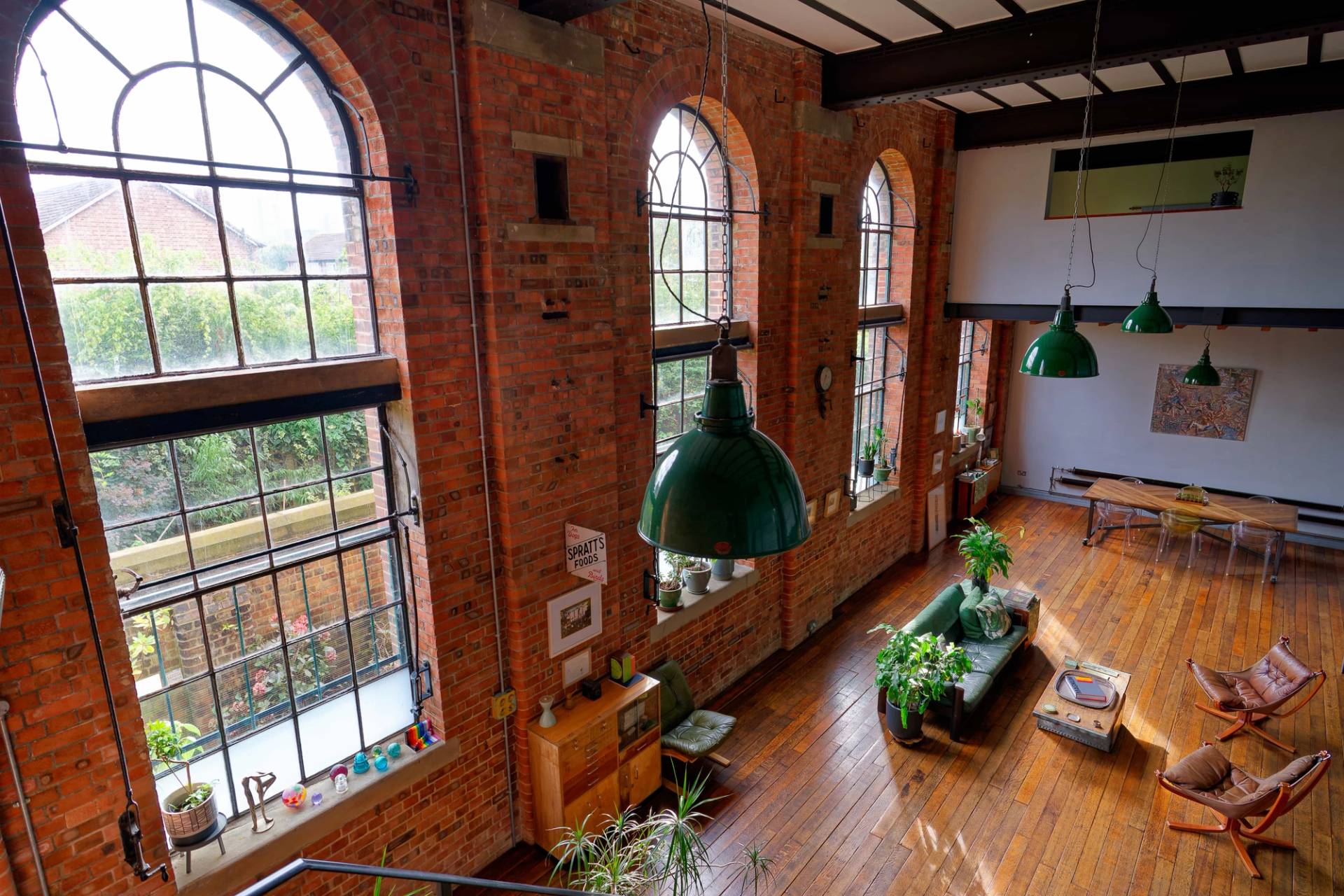 High-angle perspective of double-height arched warehouse windows framing green pendant lights and exposed red brickwork, Love Locations E14.