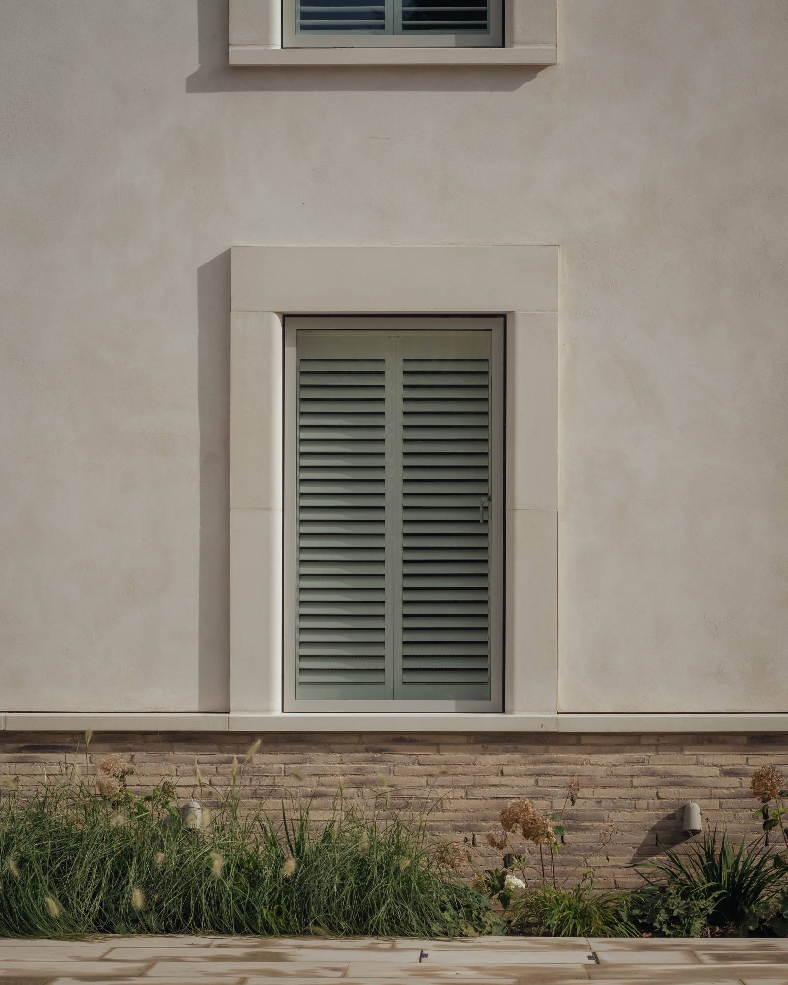 Detailed view of a modern window frame with integrated white louvered shutters set into a lime-plaster facade, Love Locations.