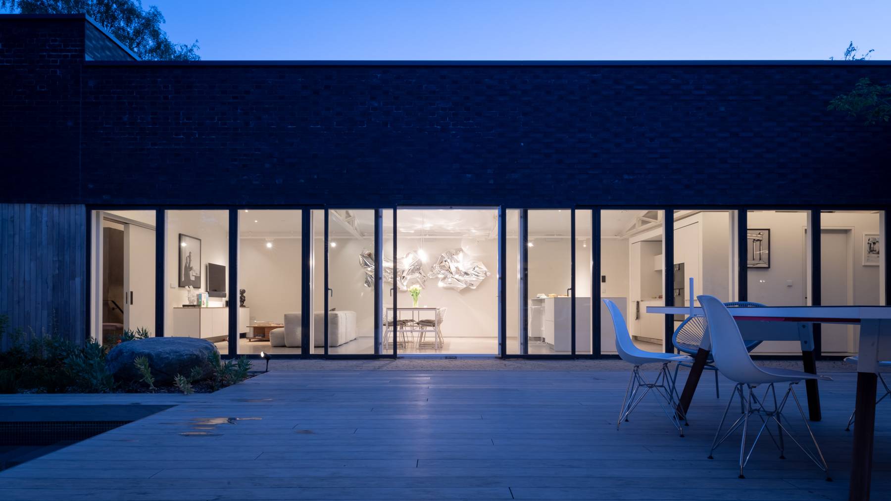 Illuminated twilight view of a modern single-storey home with full-height sliding glass doors and deck, Love Locations BN3.