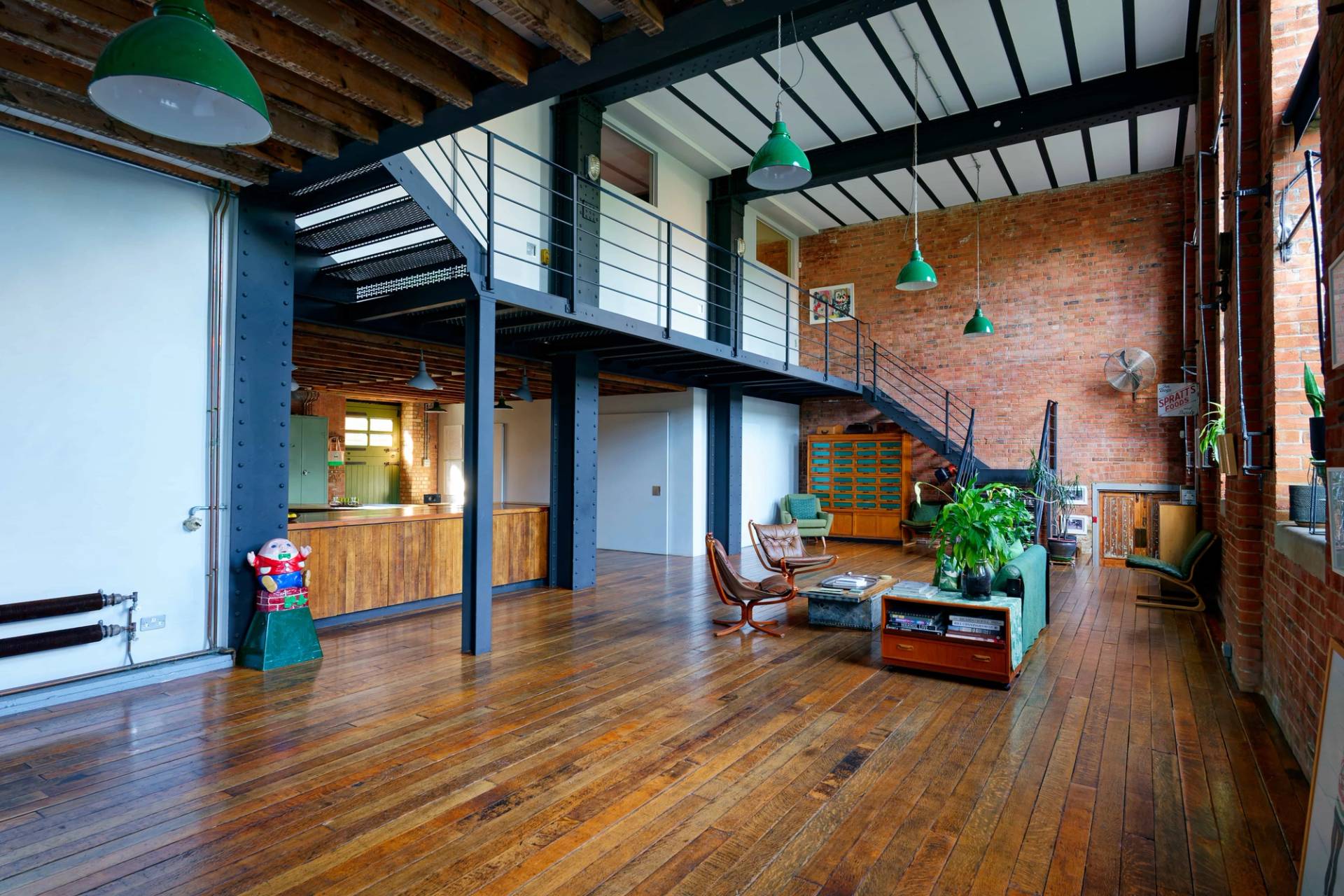 Warehouse loft view showing black steel staircase leading to a mezzanine level set against exposed red brick walls, Love Locations E14.