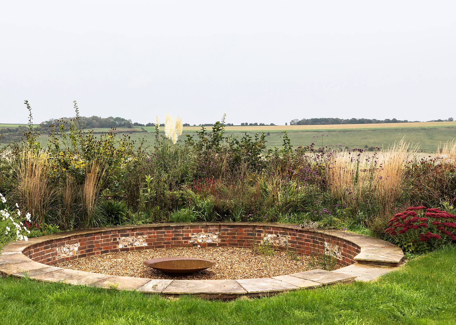 Sunken stone fire pit area set in a gravel garden overlooking open Wiltshire countryside, Love Locations SN8.