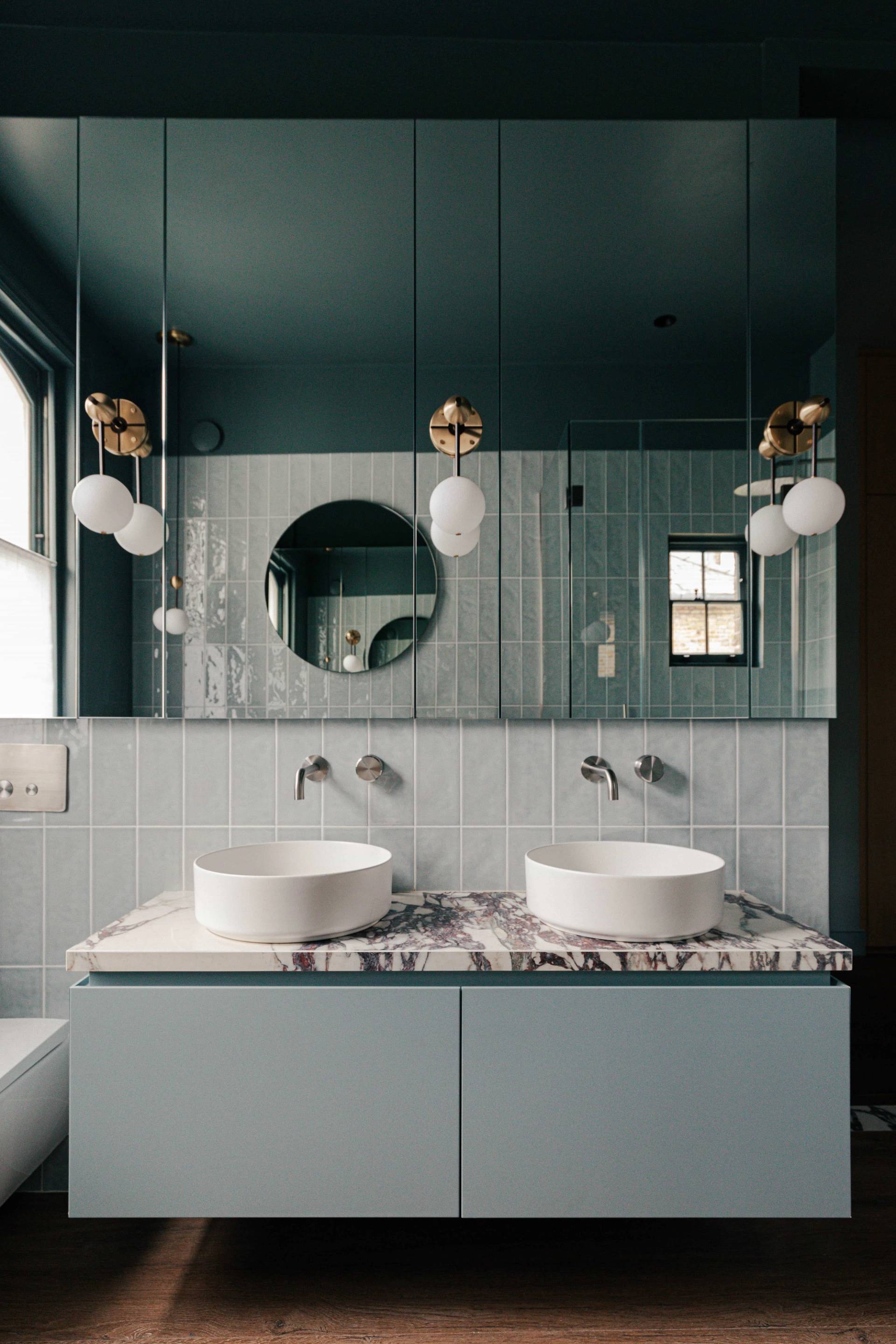 Double marble sink vanity with brass taps, round mirrors, and teal tiled walls in a luxury SW13 home, Love Locations.