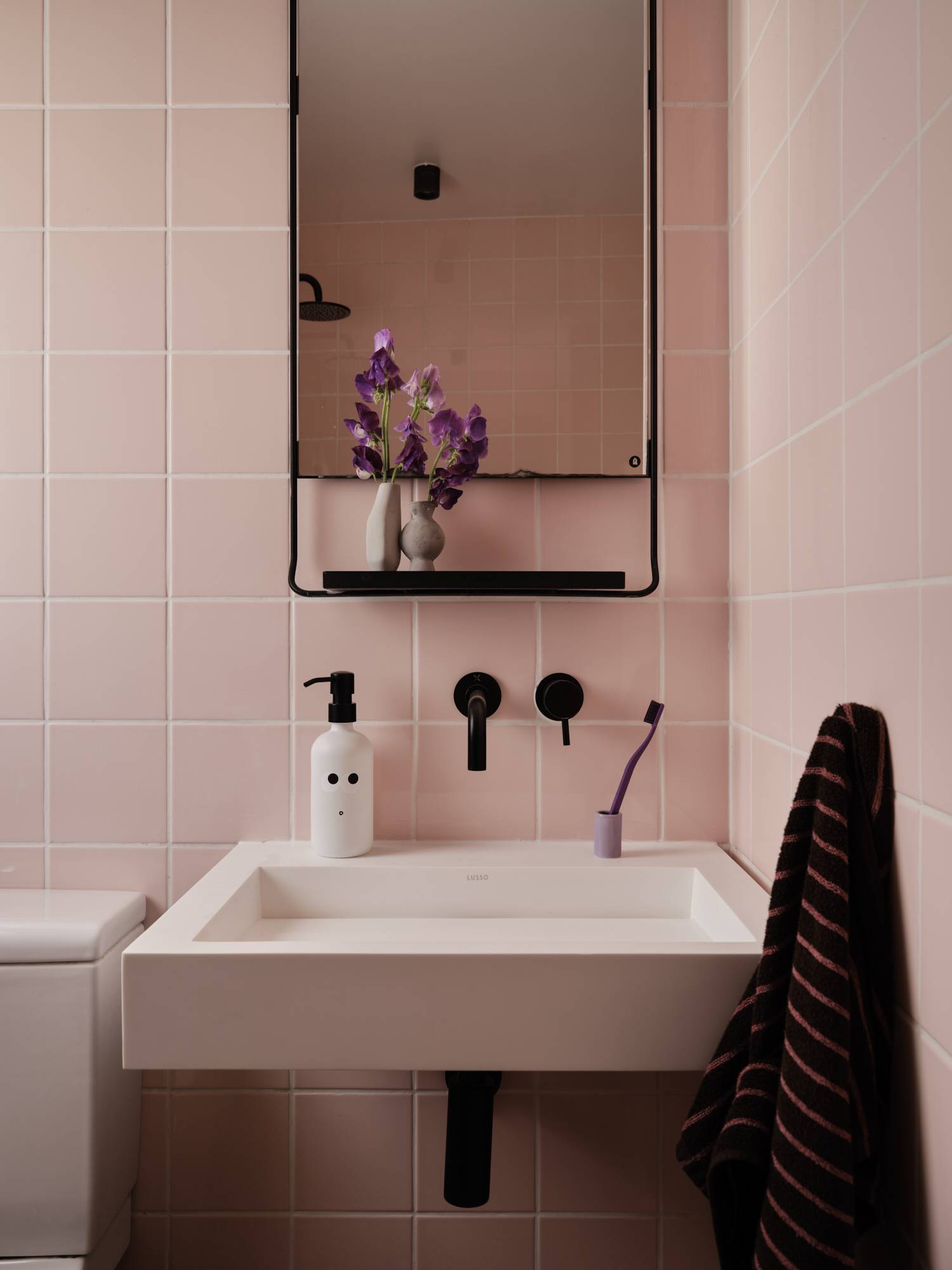 Love Locations pastel pink bathroom SE23: High-end washroom showcasing a modern square basin against square pink tiles, matte black fixtures, and a black mirror frame, ideal for beauty commercials.
