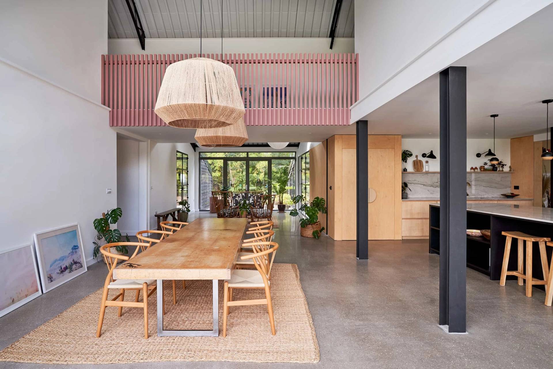Double-height open-plan dining room with pink corrugated balcony trim, long timber table, and polished concrete floors, Love Locations IP30.