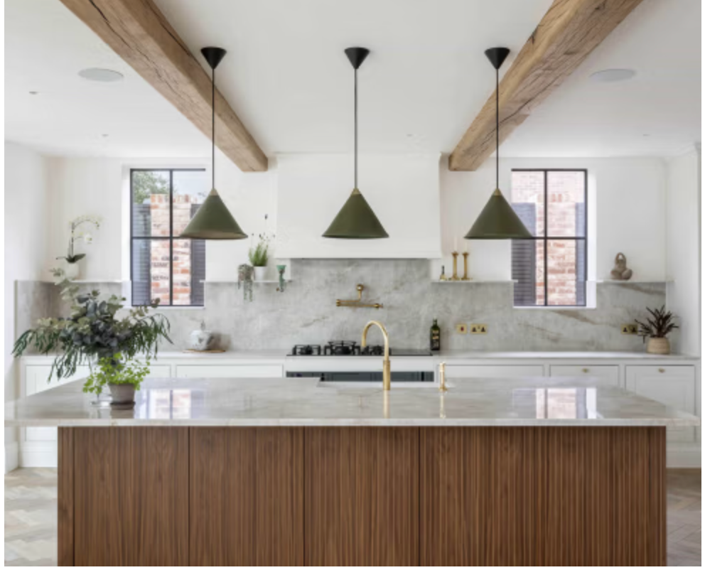 Contemporary kitchen at Badgers Drift featuring a large marble island, fluted wood cabinetry, exposed oak beams, marble splashback, brass tap, and statement green pendant lights in a bright open-plan space.