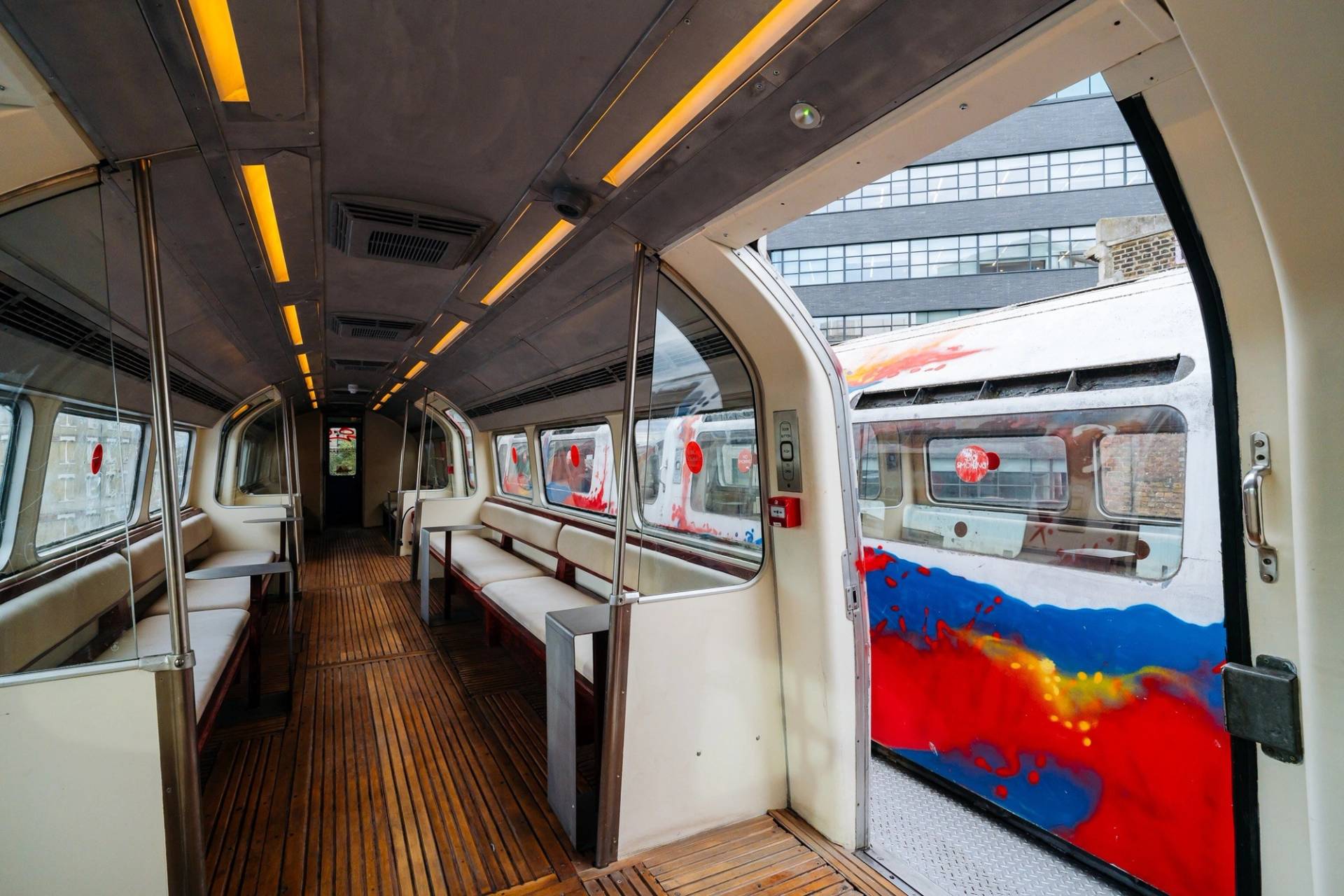 Inside view of a refurbished vintage tube carriage venue hire with wooden flooring, warm ceiling strip lighting, and city backdrop views through Love Locations.