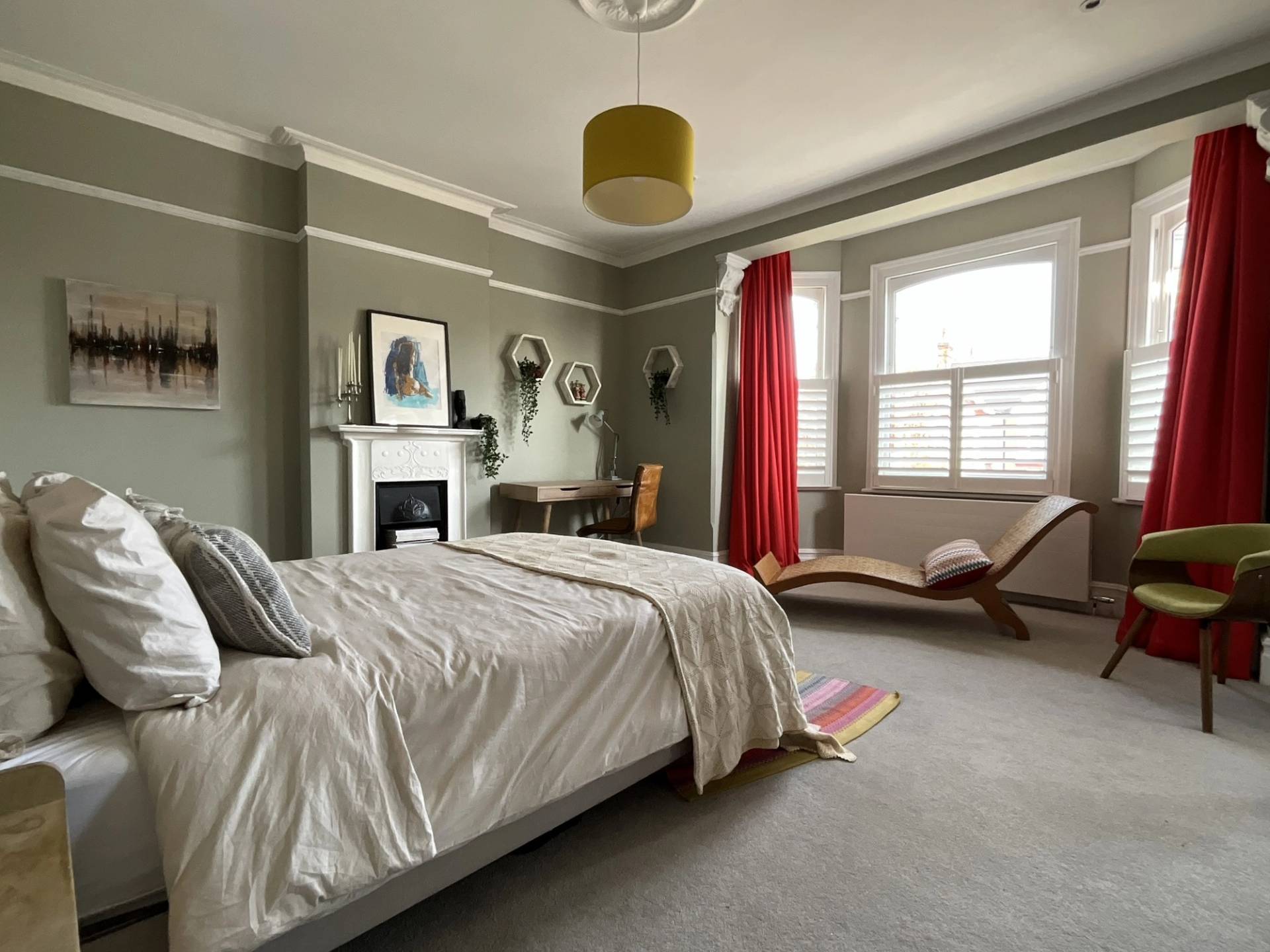 Master bedroom setup with red window drapes, wooden chaise lounge, olive green walls, and full-length floor mirror, Love Locations Ealing Common.