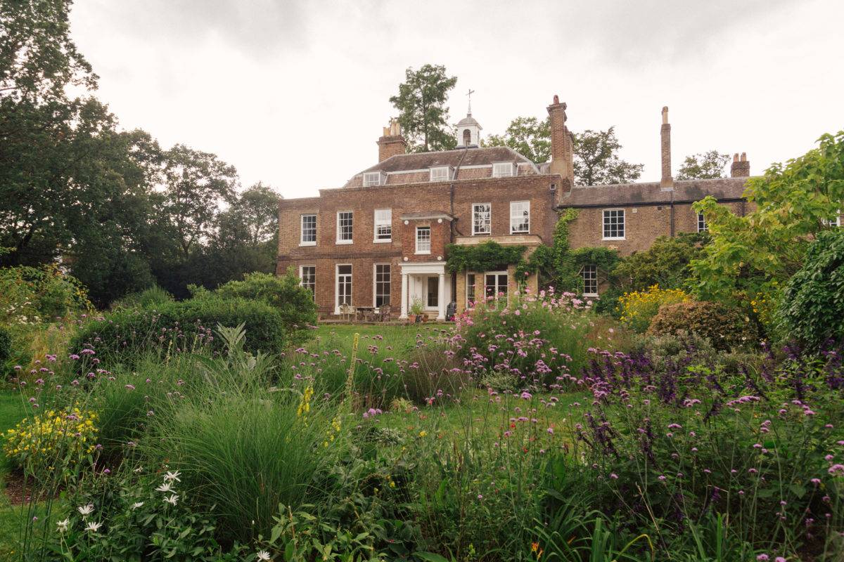 Rear garden view of a red brick period mansion surrounded by vibrant flower beds and climbing vines, Love Locations.