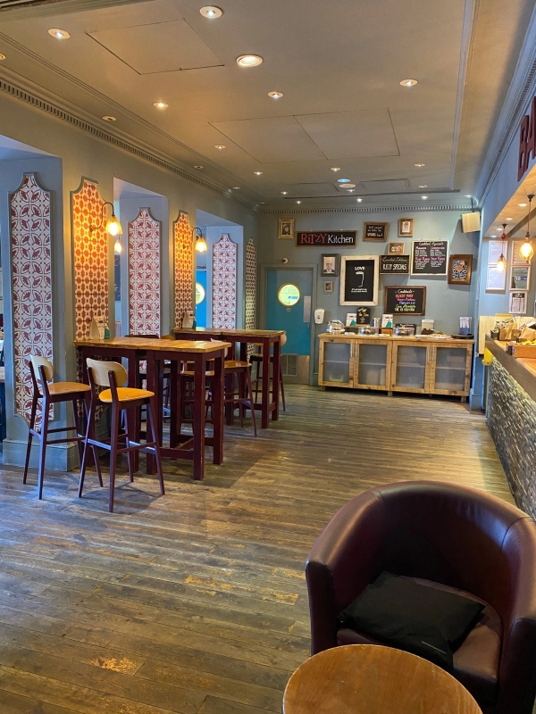 Spacious seating area with decorative wallpaper accents, high-top tables, and leather armchairs inside The Ritzy Cafe filming location in Brixton SW2 by Love Locations.