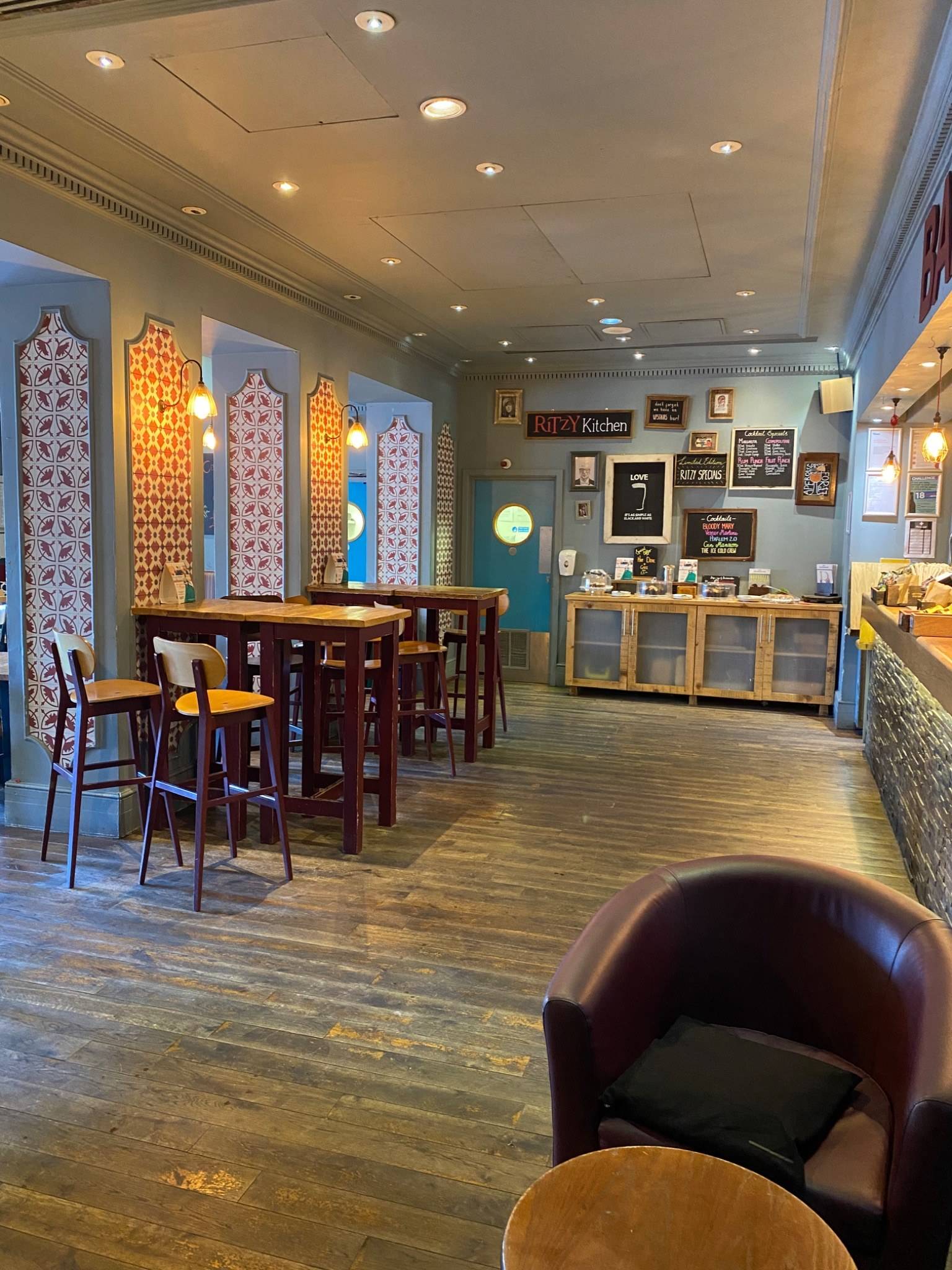 Spacious seating area with decorative wallpaper accents, high-top tables, and leather armchairs inside The Ritzy Cafe filming location in Brixton SW2 by Love Locations.