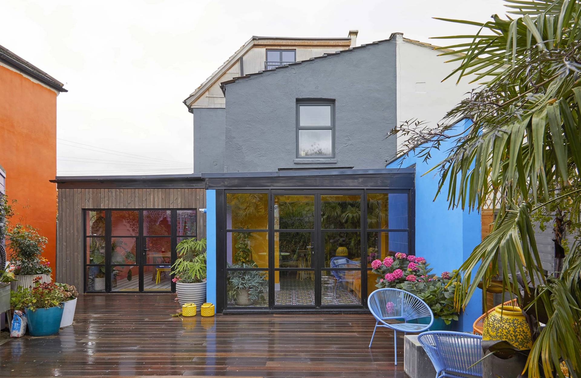 Modern grey and blue house rear facade with large black glass patio doors opening onto timber decking, Love Locations SE6.