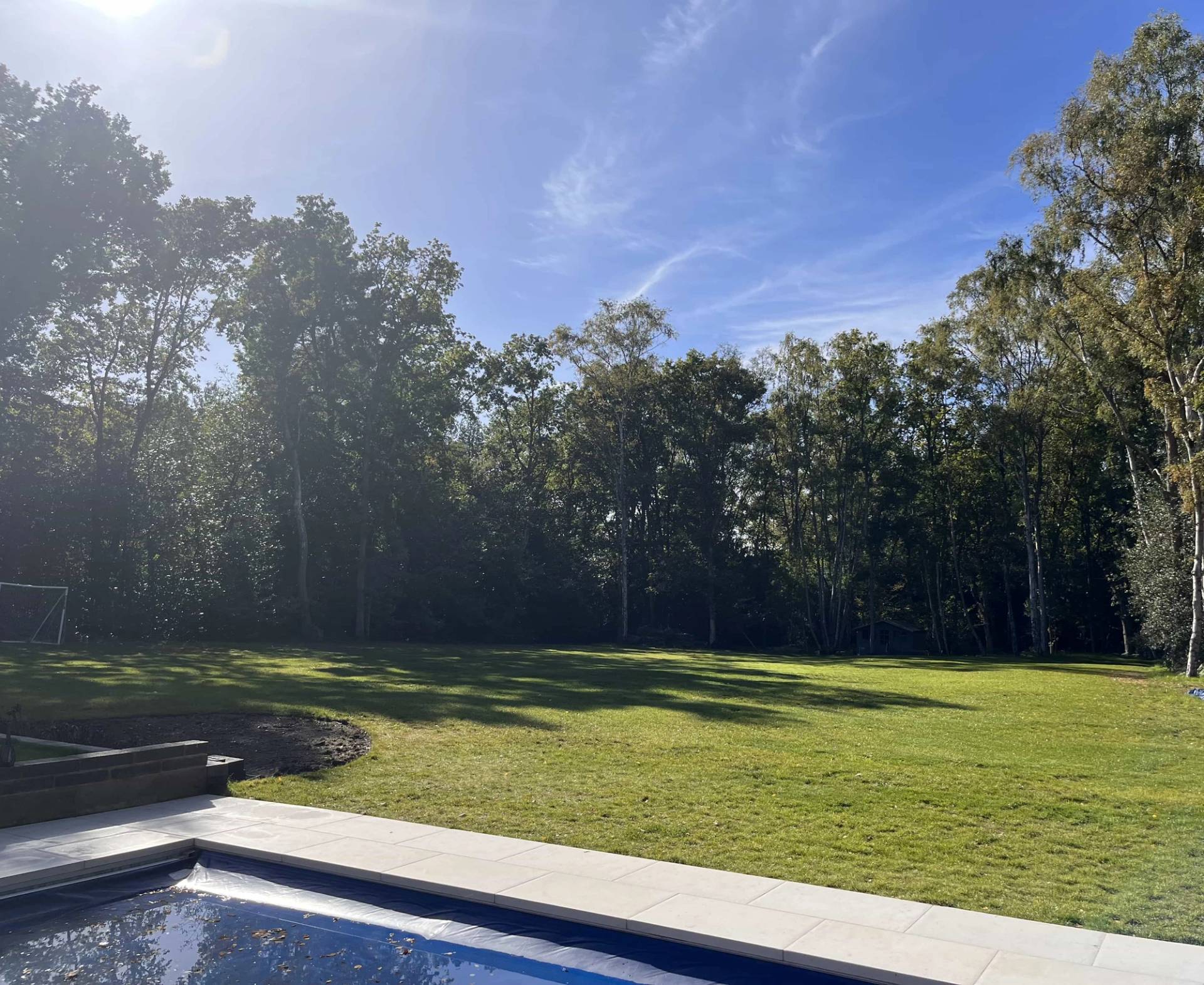 Expansive manicured lawn garden overlooking an outdoor swimming pool and surrounding woodland trees, Love Locations GU3.