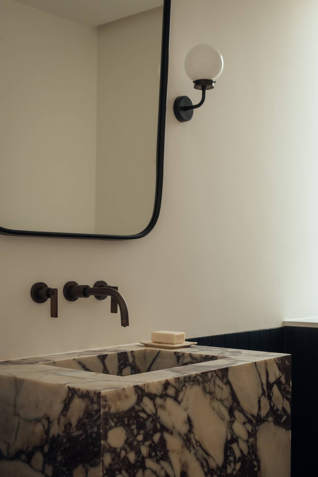 Luxury marble washbasin detailed with black wall-mounted tapware and a minimalist rounded mirror, ideal for premium bathroom fixture marketing, Love Locations.