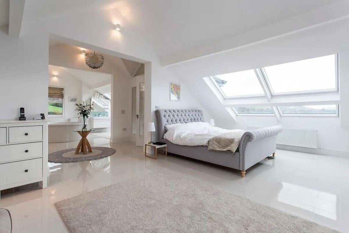 Modern attic bedroom film location in Stockport SK6 from Love Locations, displaying sloped ceilings with skylights, light tiled flooring, and neutral decor.