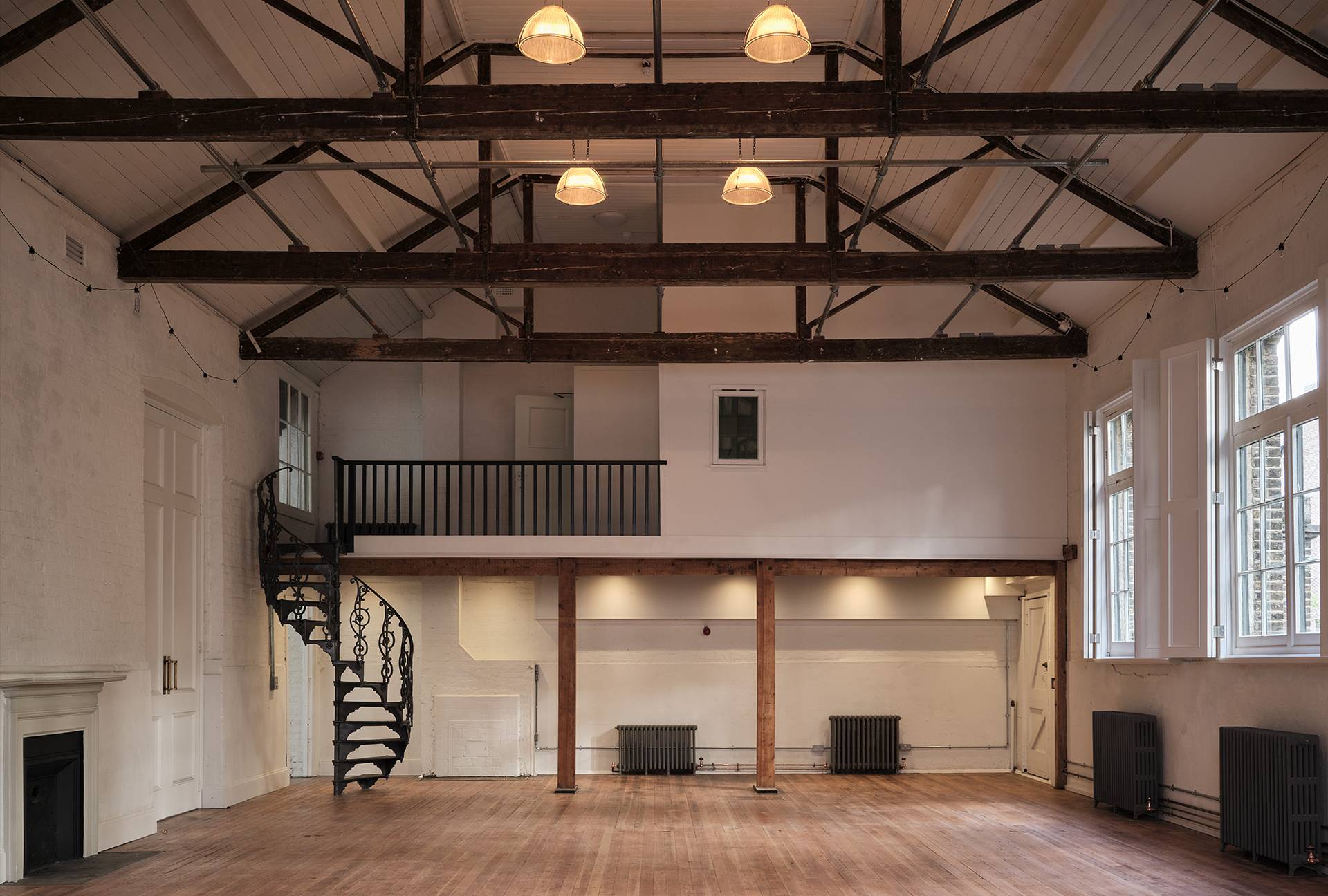 Spacious double-height event hall shoot location in Shoreditch, E2 featuring vaulted roof trusses, spiral staircase, and original timber floors via Love Locations.