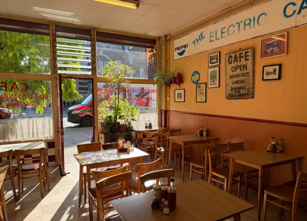 Retro cafe dining area featuring wooden tables, chairs, vintage wall signs, and large window frontage, Love Locations SE27.