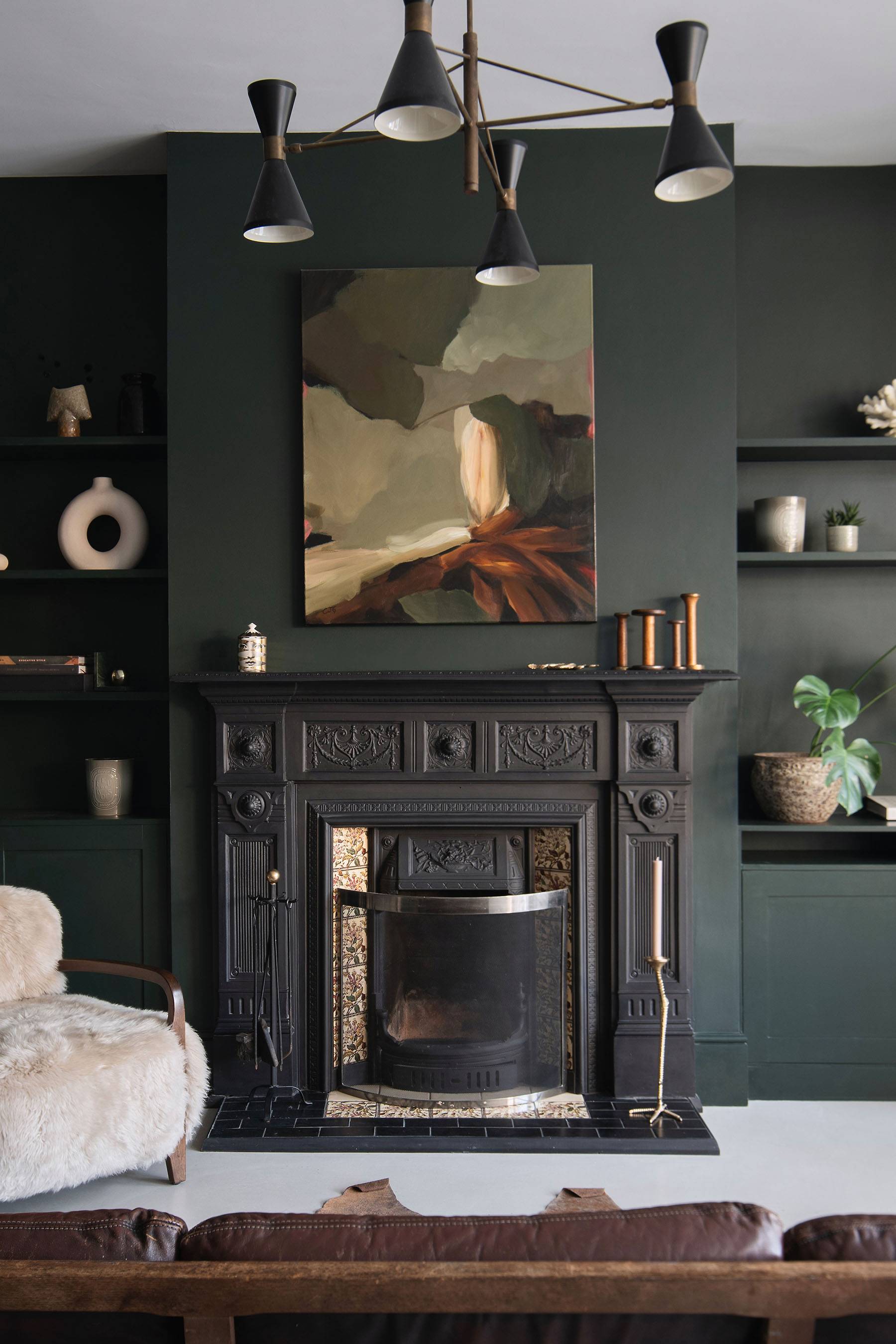 Close-up of a period cast iron fireplace set against dark green walls with modern ceramics on display, Love Locations SW16.