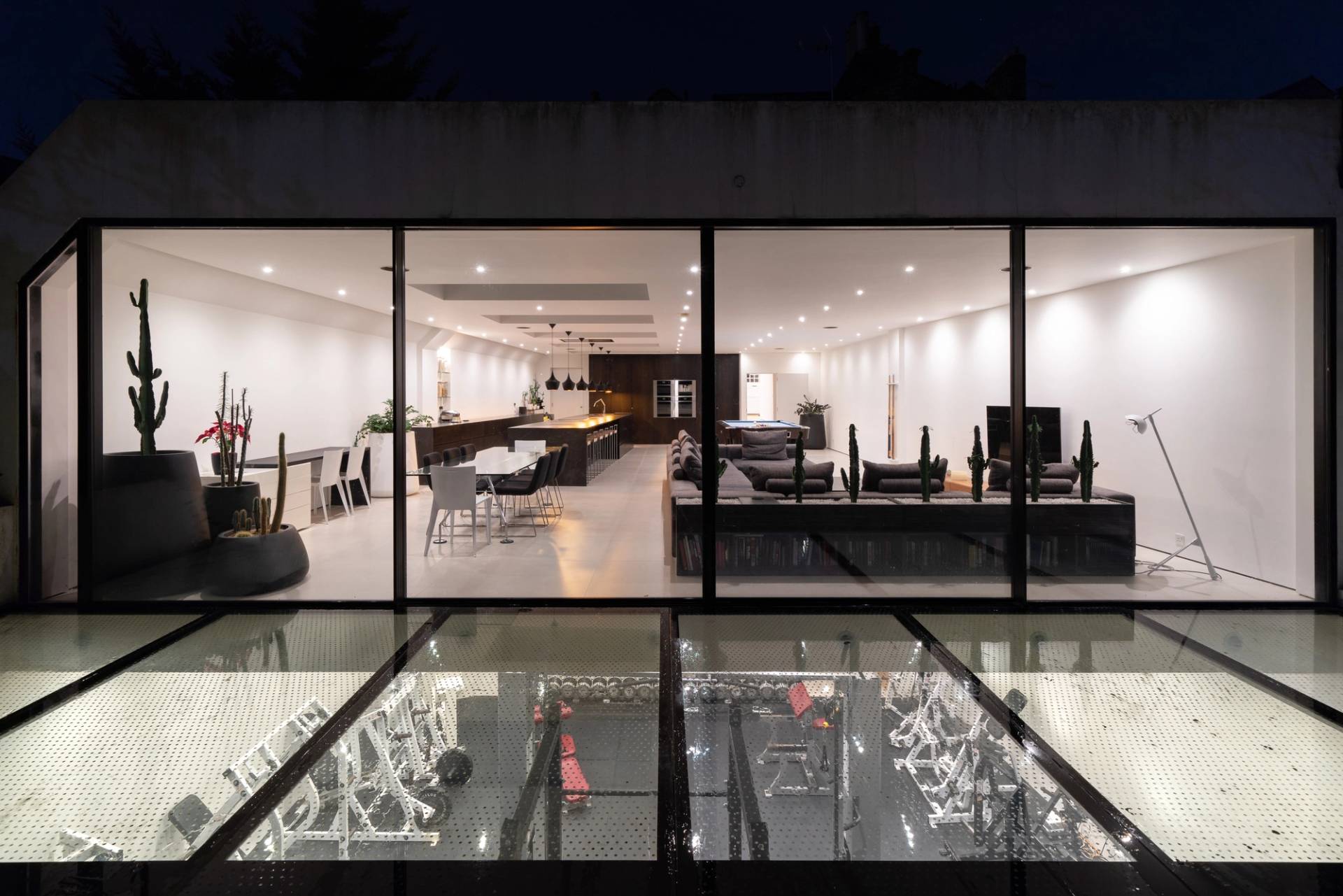 Exterior courtyard glass floor looking down into an illuminated subterranean home gym at night, Love Locations SW6.