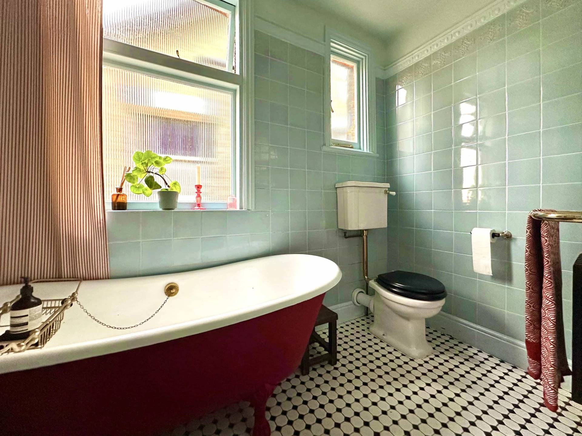 Period bathroom with red freestanding roll-top bathtub, black-and-white tiled floor, and high-tank WC, Love Locations N13.