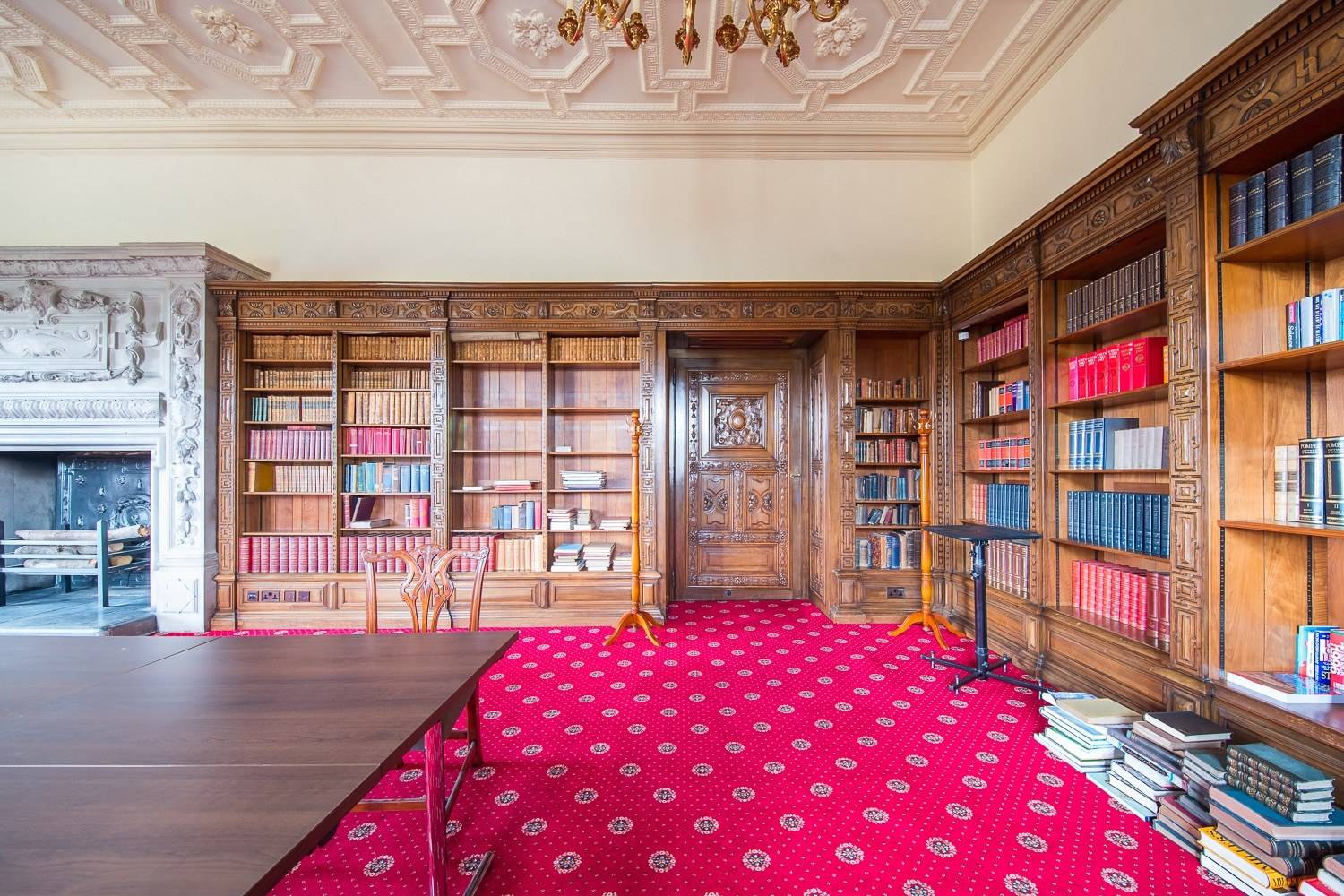 Traditional country house library shoot space with dark wood bookcases, red carpet, and brass chandelier via Love Locations.