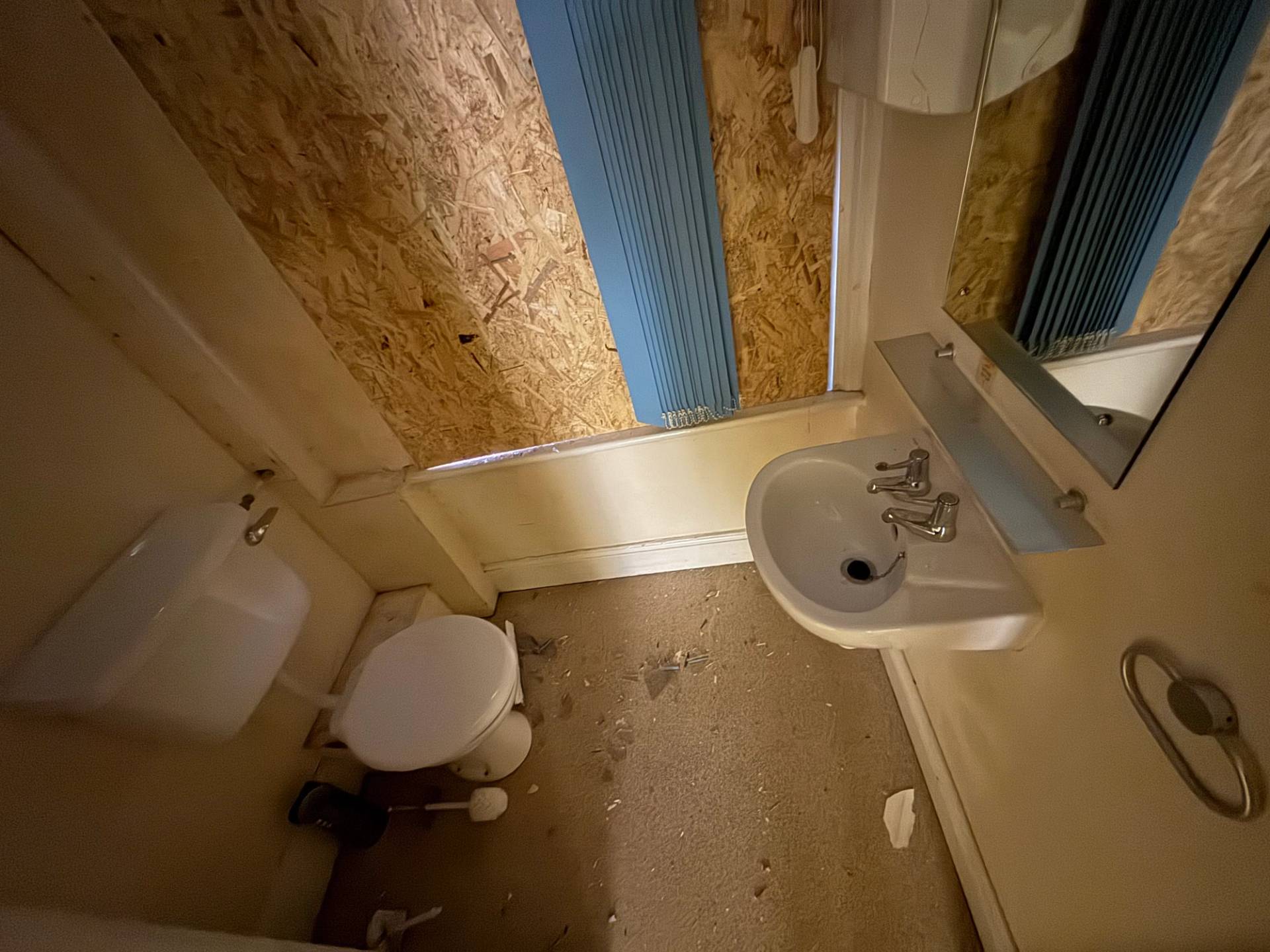 High-angle look at a dirty, abandoned toilet and washbasin with a plywood window block, curated by Love Locations.