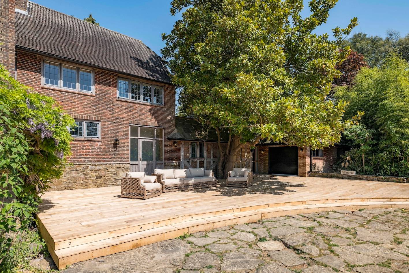 Paved outdoor stone patio terrace with luxury outdoor sofas set against a red brick house facade, Love Locations RH13.