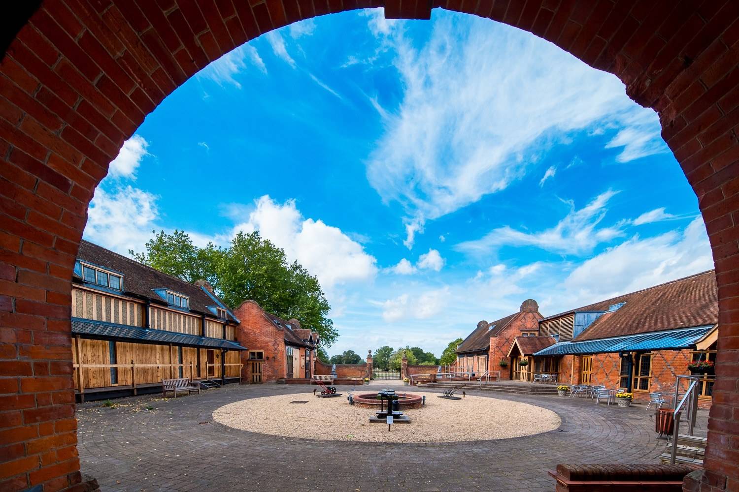Brick courtyard and outbuildings entrance archway view under a clear blue sky at North Mymms Park through Love Locations.