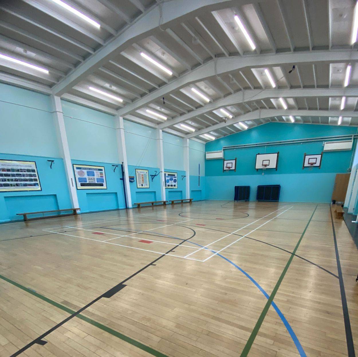 Wide view of a multi-court school gymnasium shoot space with timber floors and sports markings via Love Locations.