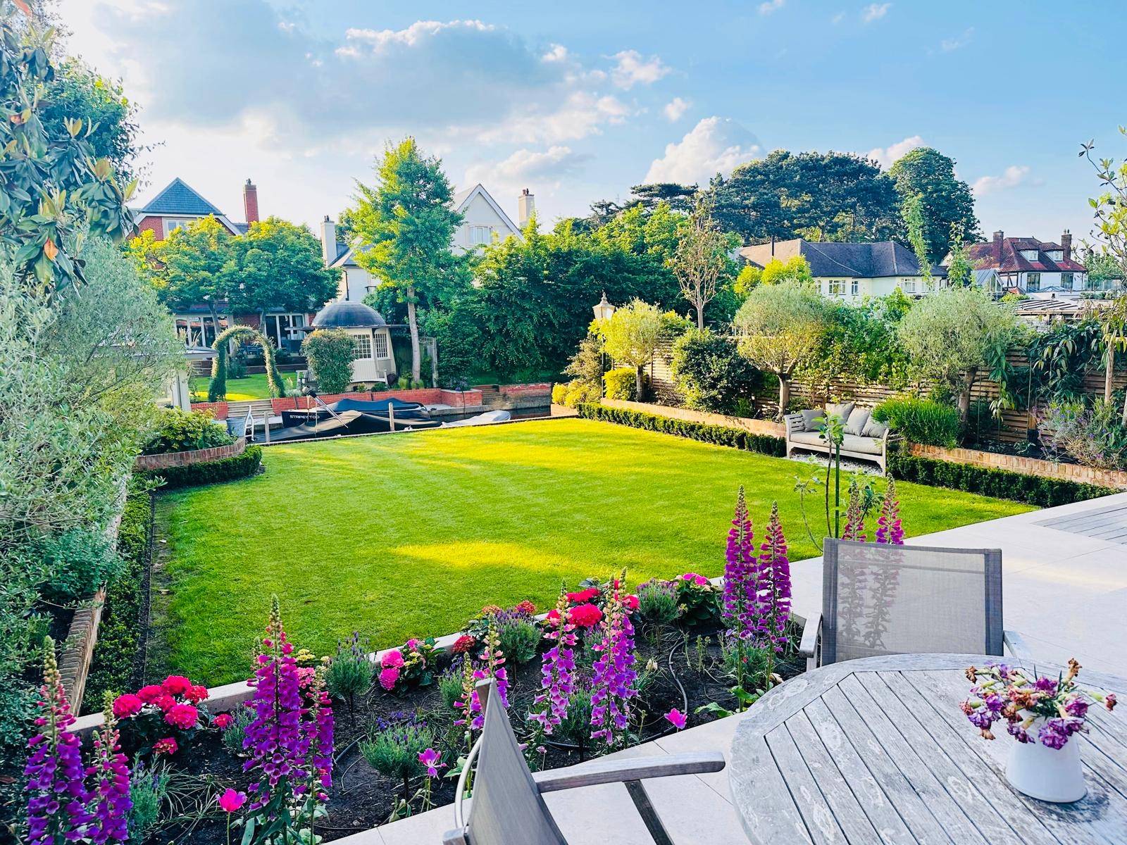 Landscaped rear garden featuring manicured lawns, flower borders, and a garden room outbuilding, Love Locations TW11.