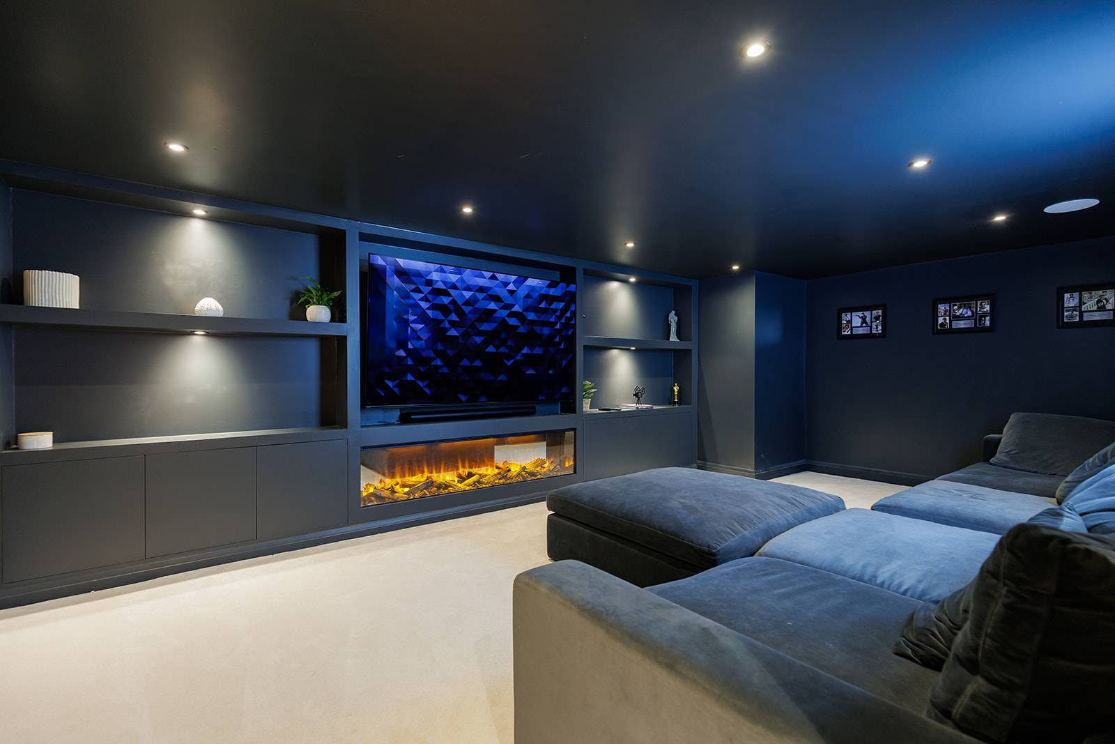 Dark moody home cinema room with plush velvet sofas, modern electric fireplace, and built-in screen wall, Love Locations RH13.