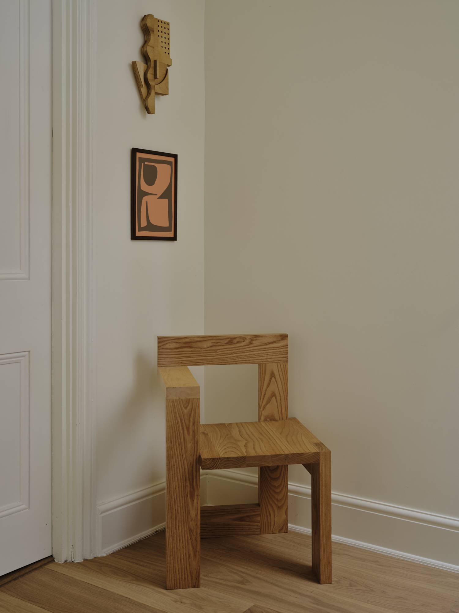 Love Locations artistic interior design location SE23: Clean corner view of a minimalist geometric oak block chair against neutral putty-toned walls, perfect for high-fashion lookbooks.