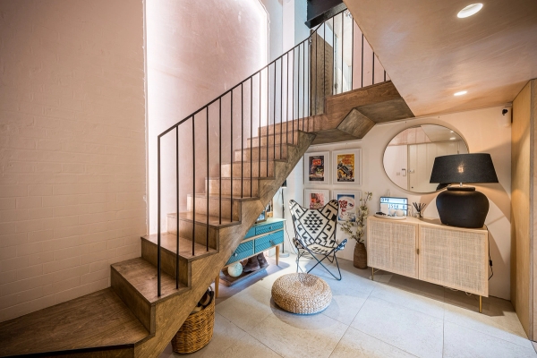 Bespoke architectural wooden staircase with a sleek black metal balustrade against a soft pink plaster feature wall, Love Locations.