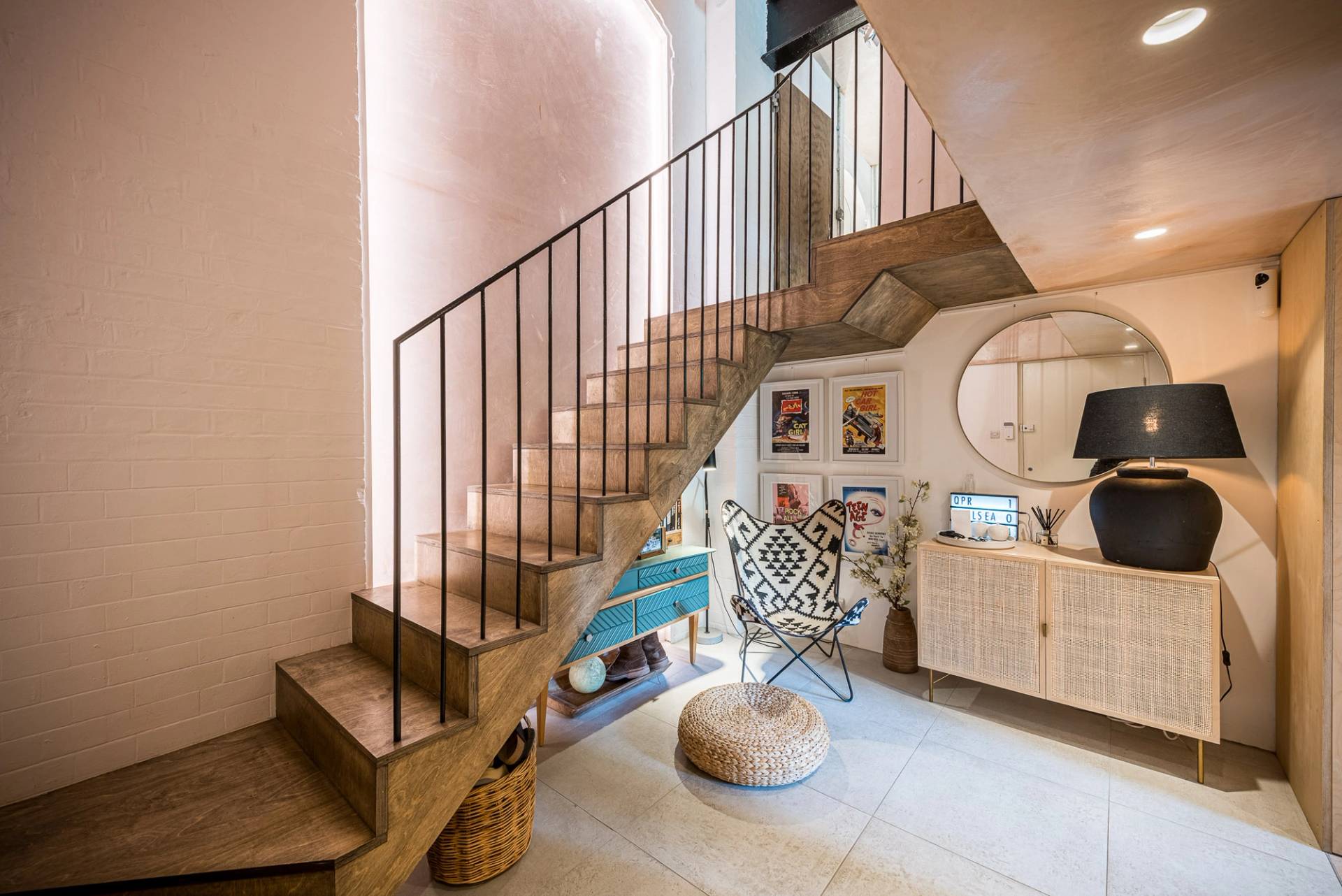 Bespoke architectural wooden staircase with a sleek black metal balustrade against a soft pink plaster feature wall, Love Locations.