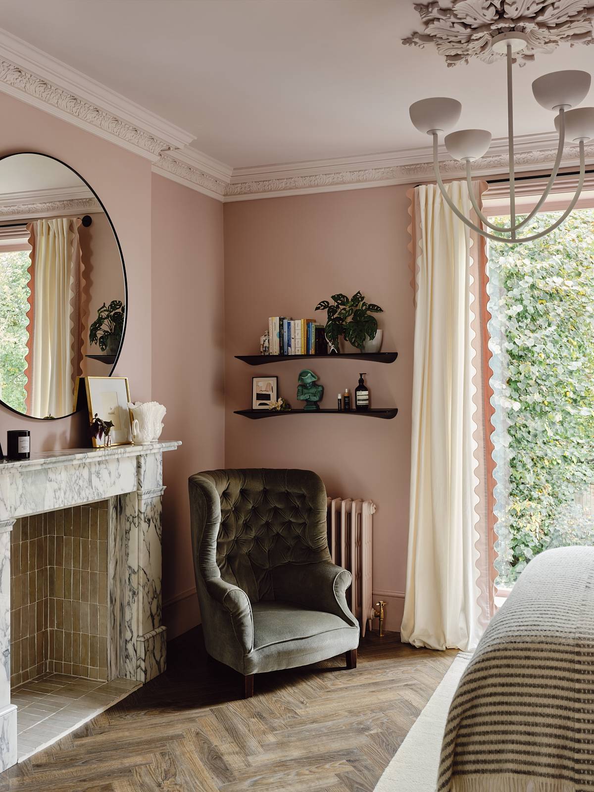 Grey marble fireplace mantel set against plaster pink walls with an green velvet armchair and round mirror, Love Locations CR0.