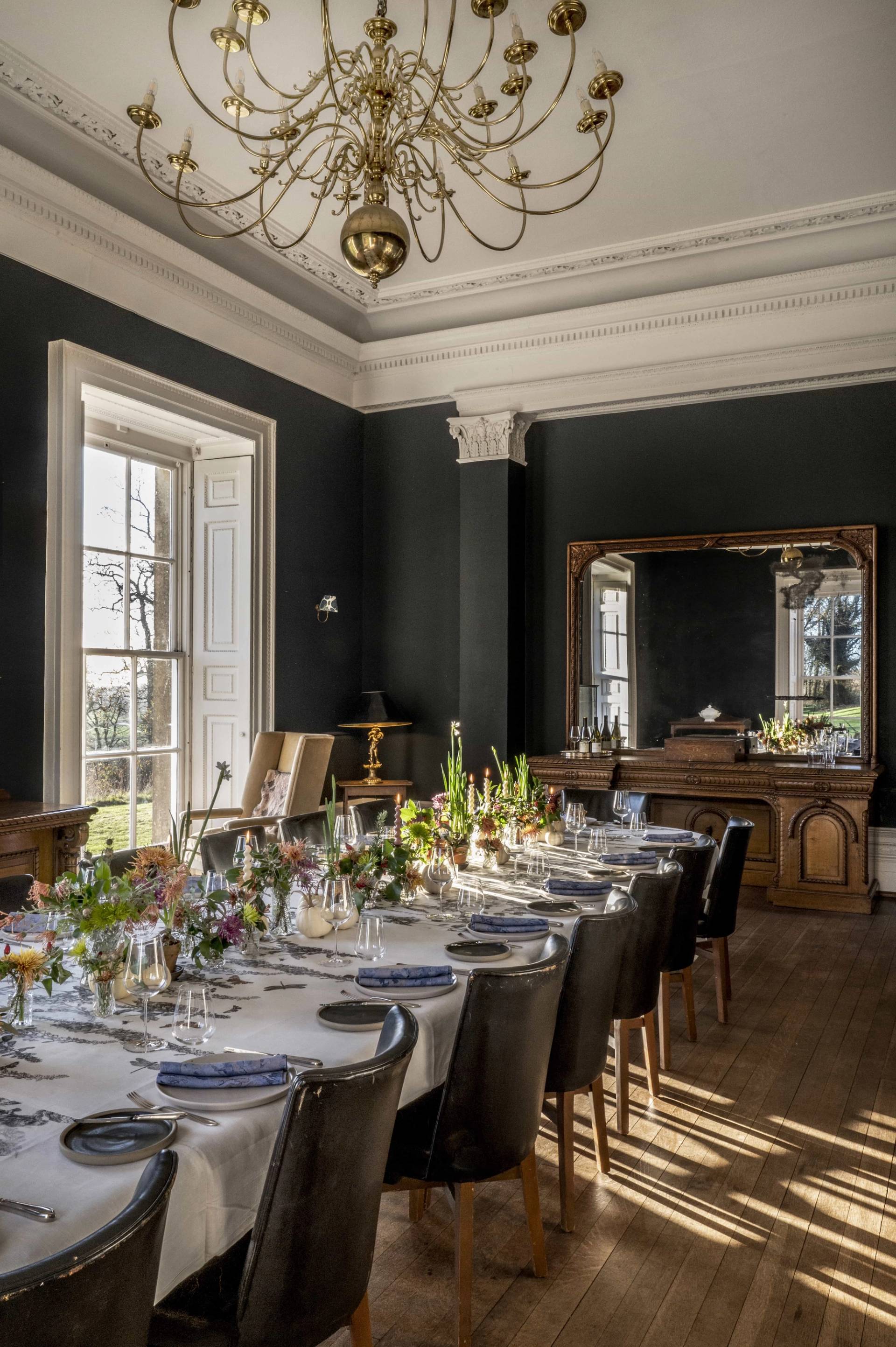 Wide shot of a formal navy dining hall showcasing a long set table, ornate mirror, and carved sideboard, ideal for period television productions, Love Locations.