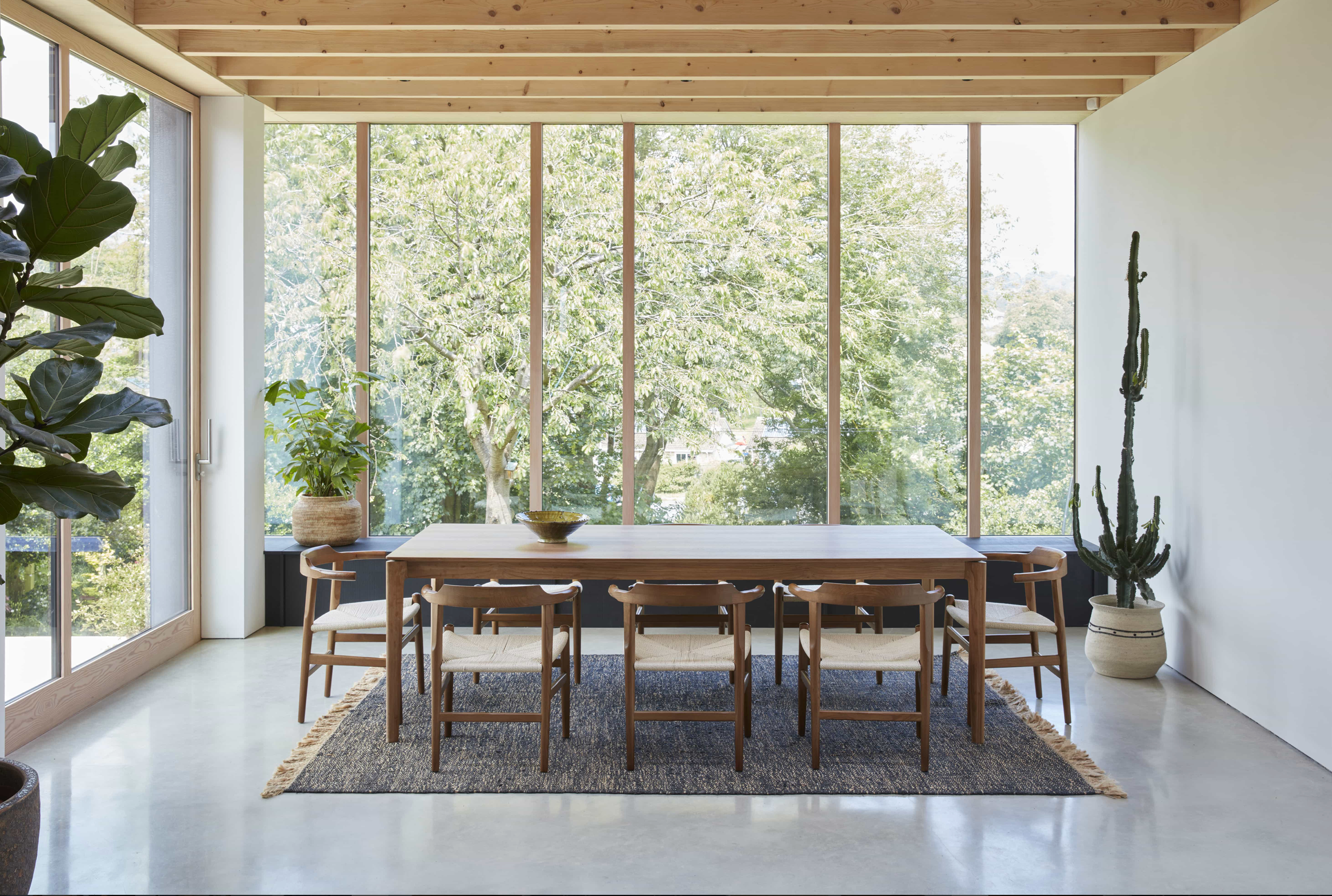 Contemporary dining room at Crescent House with floor-to-ceiling glazing, exposed timber ceiling beams and garden views.