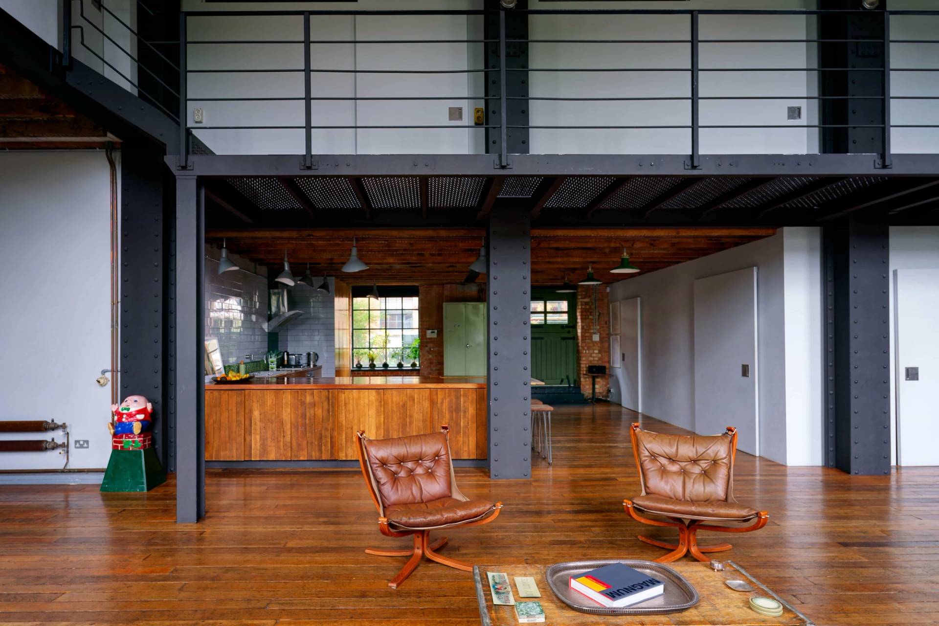 Industrial open-plan living space under steel mezzanine beams featuring warm timber floors and mid-century leather armchairs in Tower Hamlets, Love Locations E14.