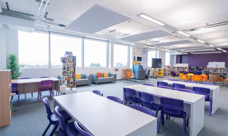 Sunlit school study hall and cafeteria space with long white tables, purple chairs, and casual lounge seating by Love Locations.