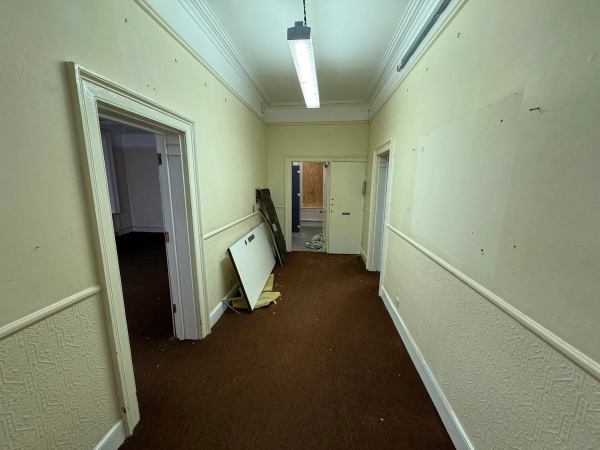 Wide institutional hallway with simple cream wainscot panel lines and open doorways for scene changes, Love Locations.