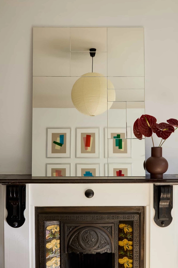 Love Locations period feature house Lewisham SE23: Traditional black mantelpiece beneath a grand mirror reflecting abstract wall art and deep red botanicals, beautiful for editorial stills.