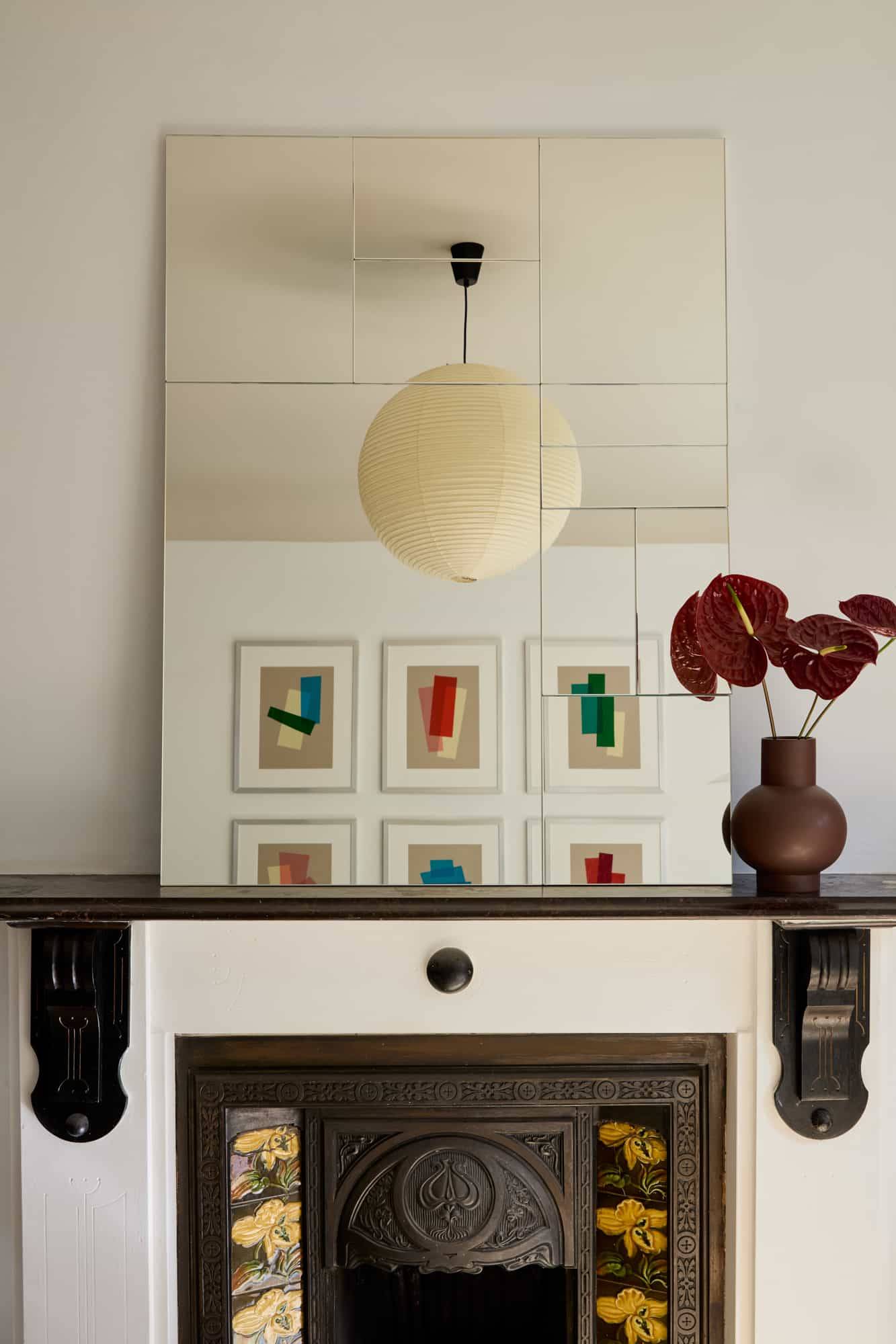 Love Locations period feature house Lewisham SE23: Traditional black mantelpiece beneath a grand mirror reflecting abstract wall art and deep red botanicals, beautiful for editorial stills.