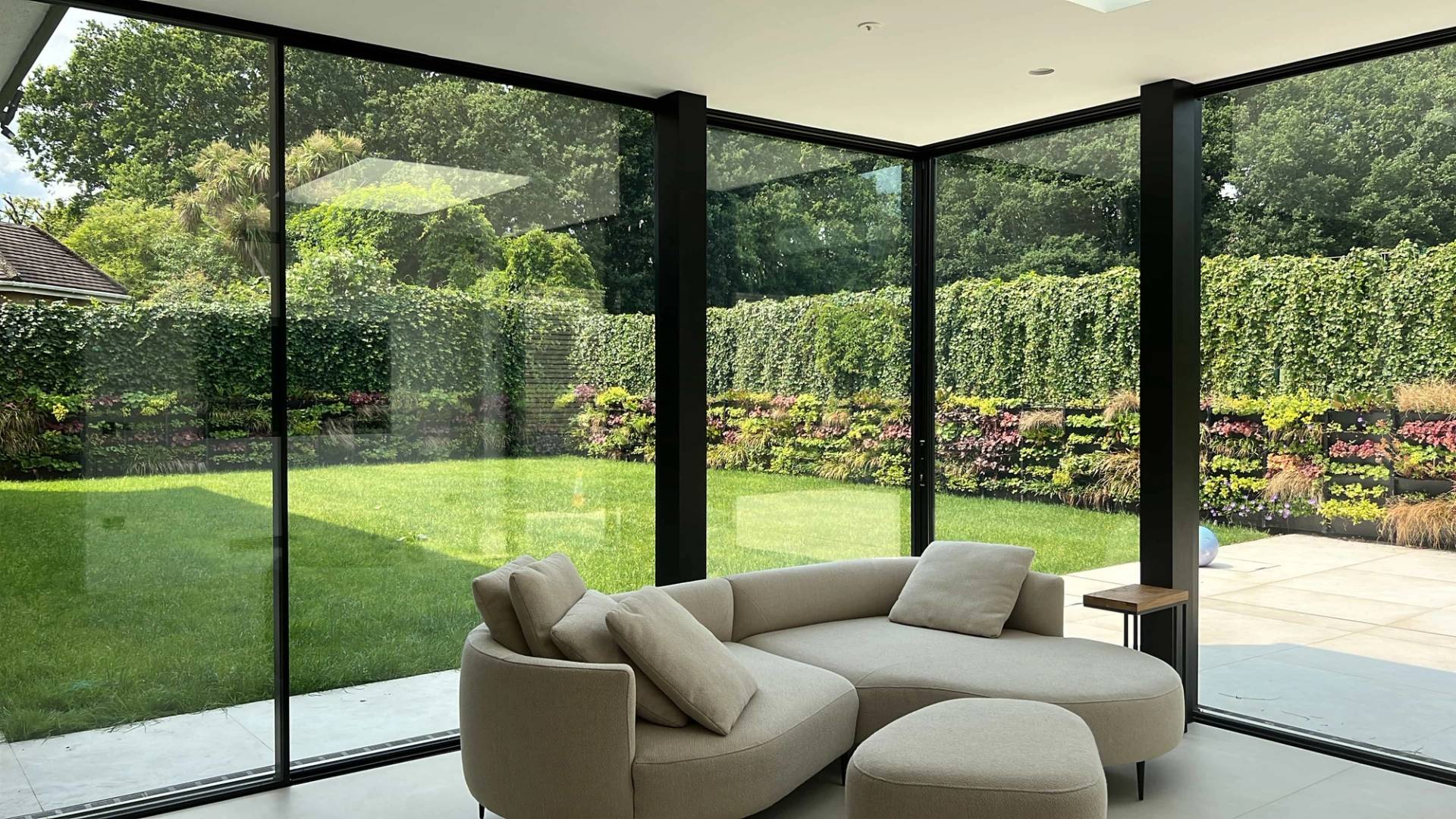 Minimalist sunroom or garden lounge featuring floor-to-ceiling corner glass walls and a neutral low-profile sofa, perfect for luxury lifestyle shoots, Love Locations.