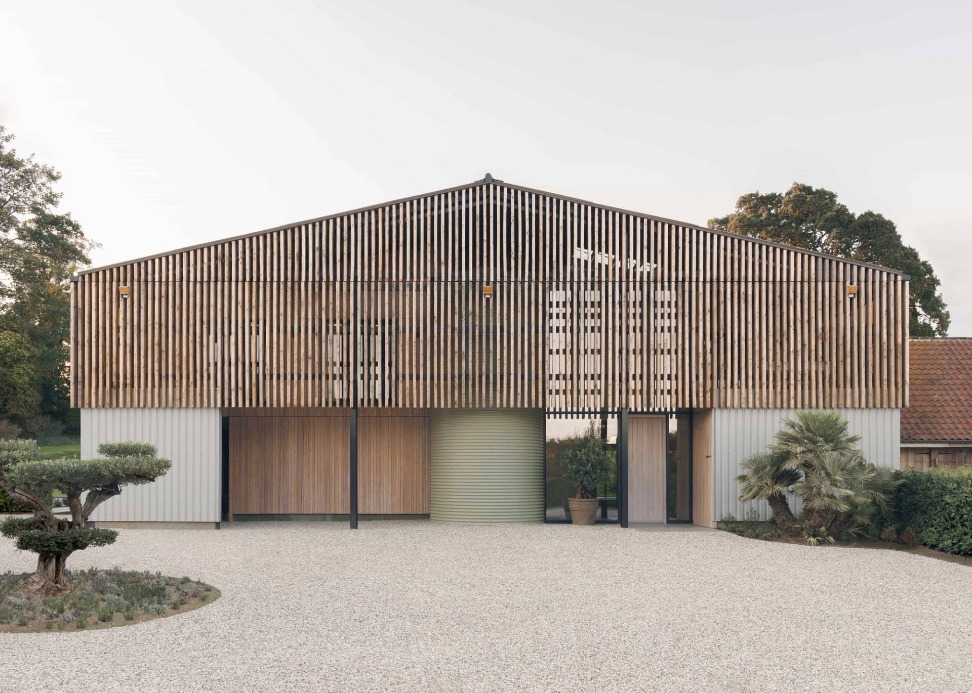 Symmetrical front elevation of a contemporary timber-slatted barn conversion with gravel driveway and green landscaping, Love Locations NR9.