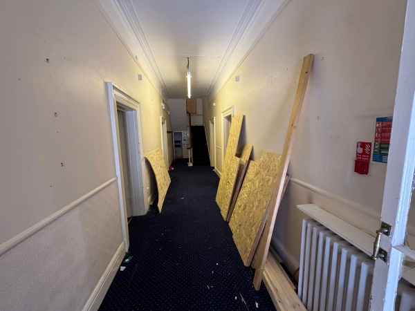 Long institutional corridor hallway with loose plywood sheets propped against cream walls in Nottingham, via Love Locations.