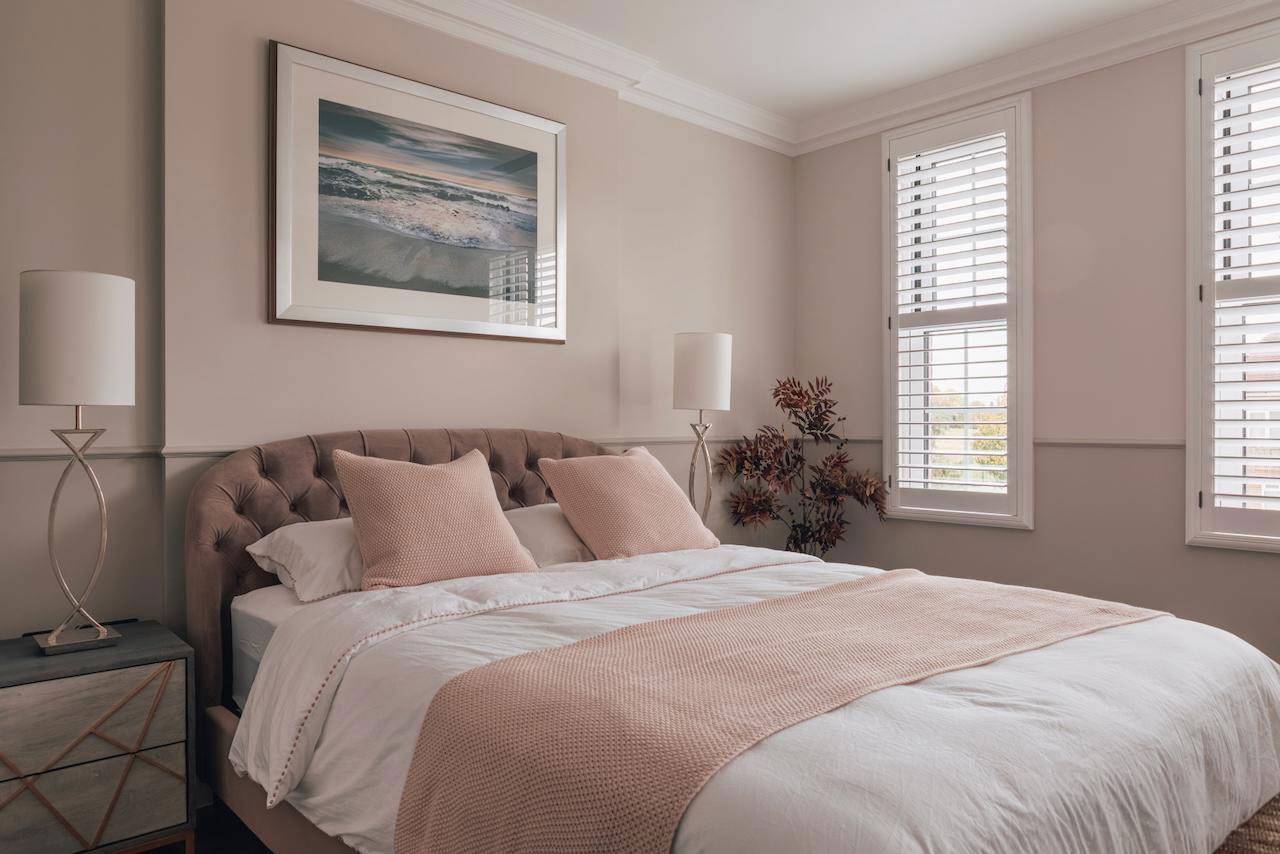 Secondary guest bedroom with soft pink bed styling, neutral walls, and sash window blinds, ideal for bedding lookbooks, Love Locations.
