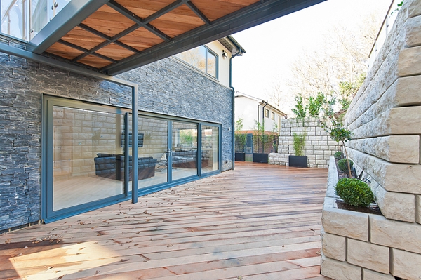 Spacious outdoor timber patio decking area enclosed by slate-grey stone facades, ideal for summer garden furniture lookbooks, Love Locations.