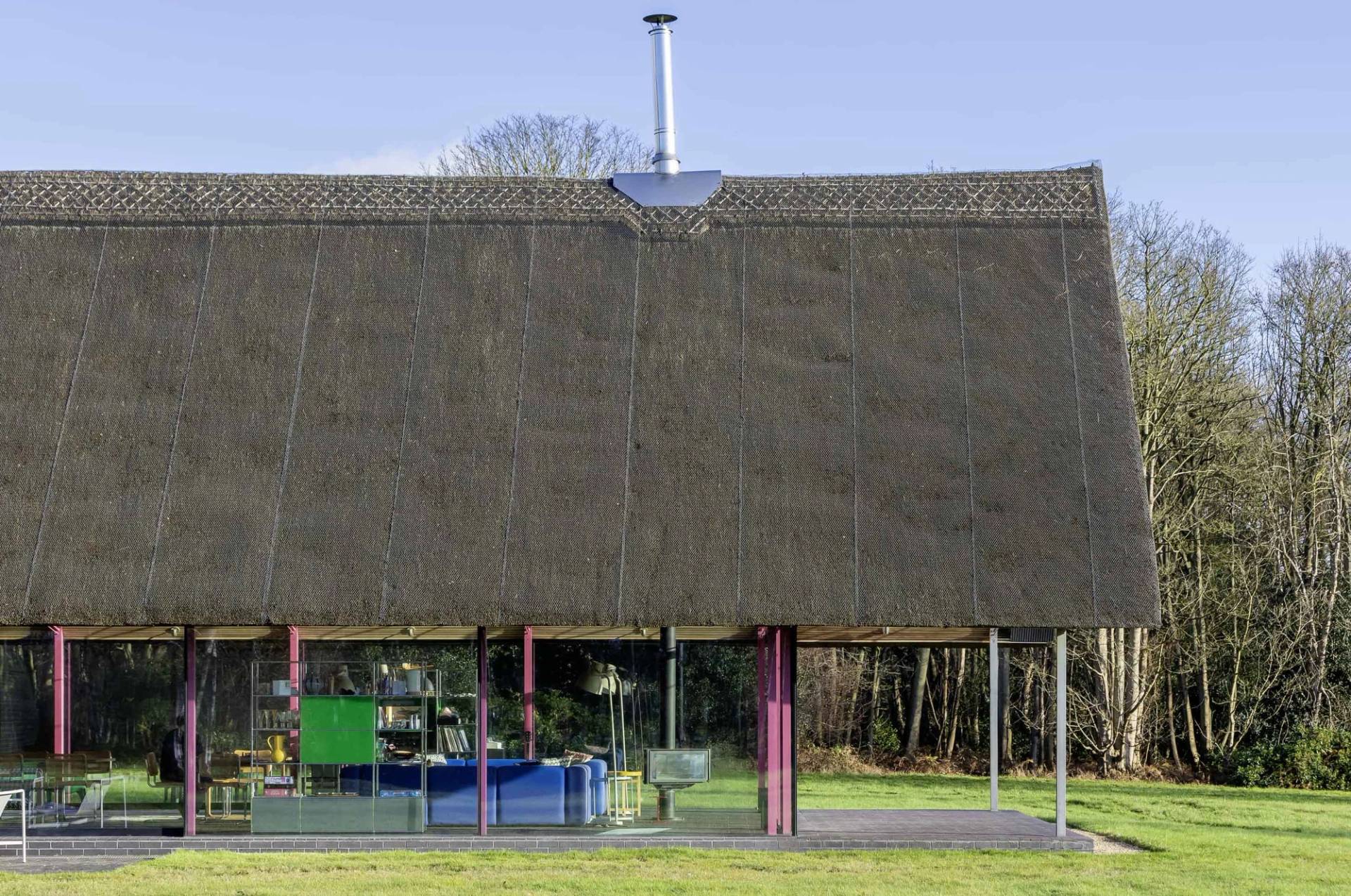 Modern thatched roof building detail showing pink steel columns and sliding glass patio doors, Love Locations IP17.